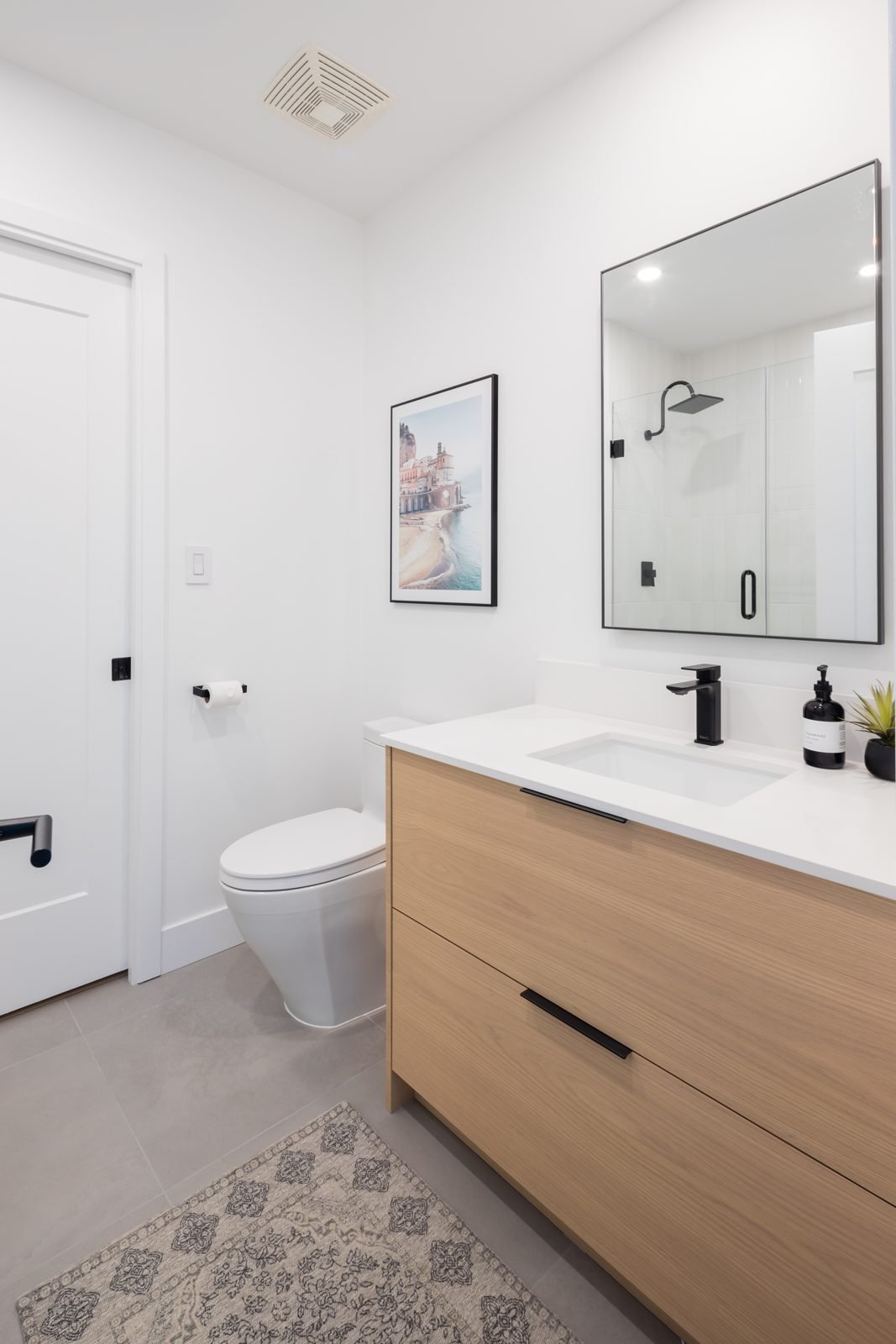 White oak vanity, black-framed mirror and one-piece toilet in a renovated Gastown condo main bathroom