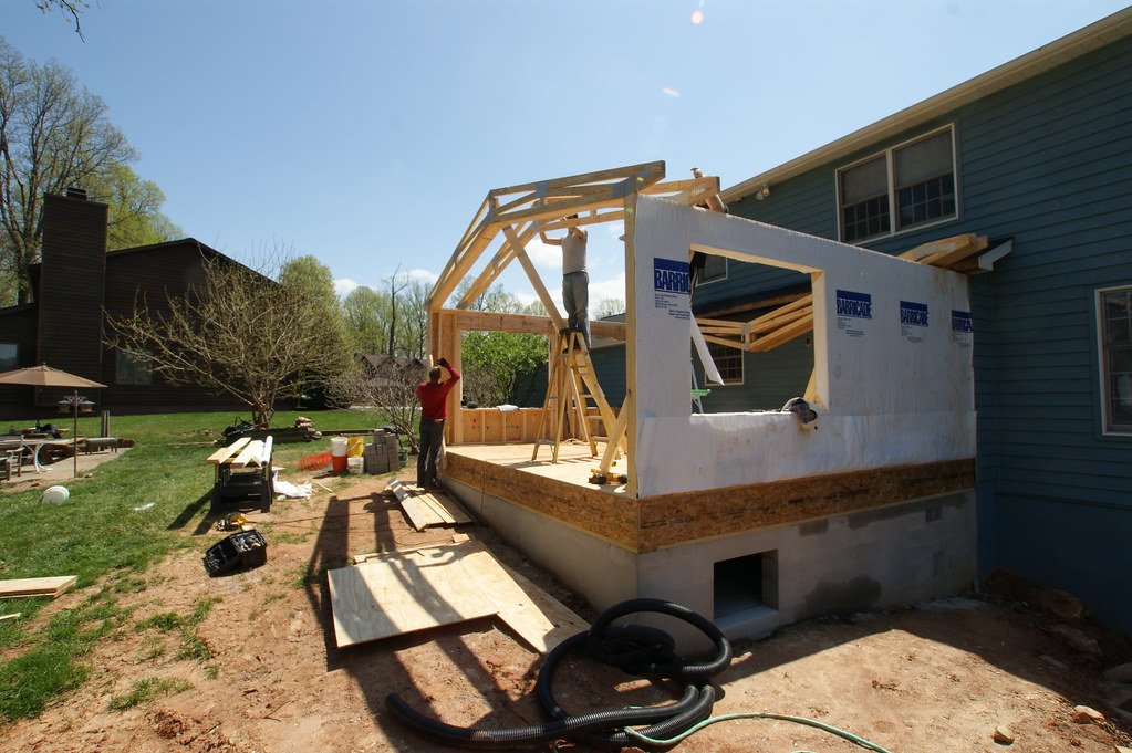 Framing for a home addition's walls and roof, with the first roof trusses being set