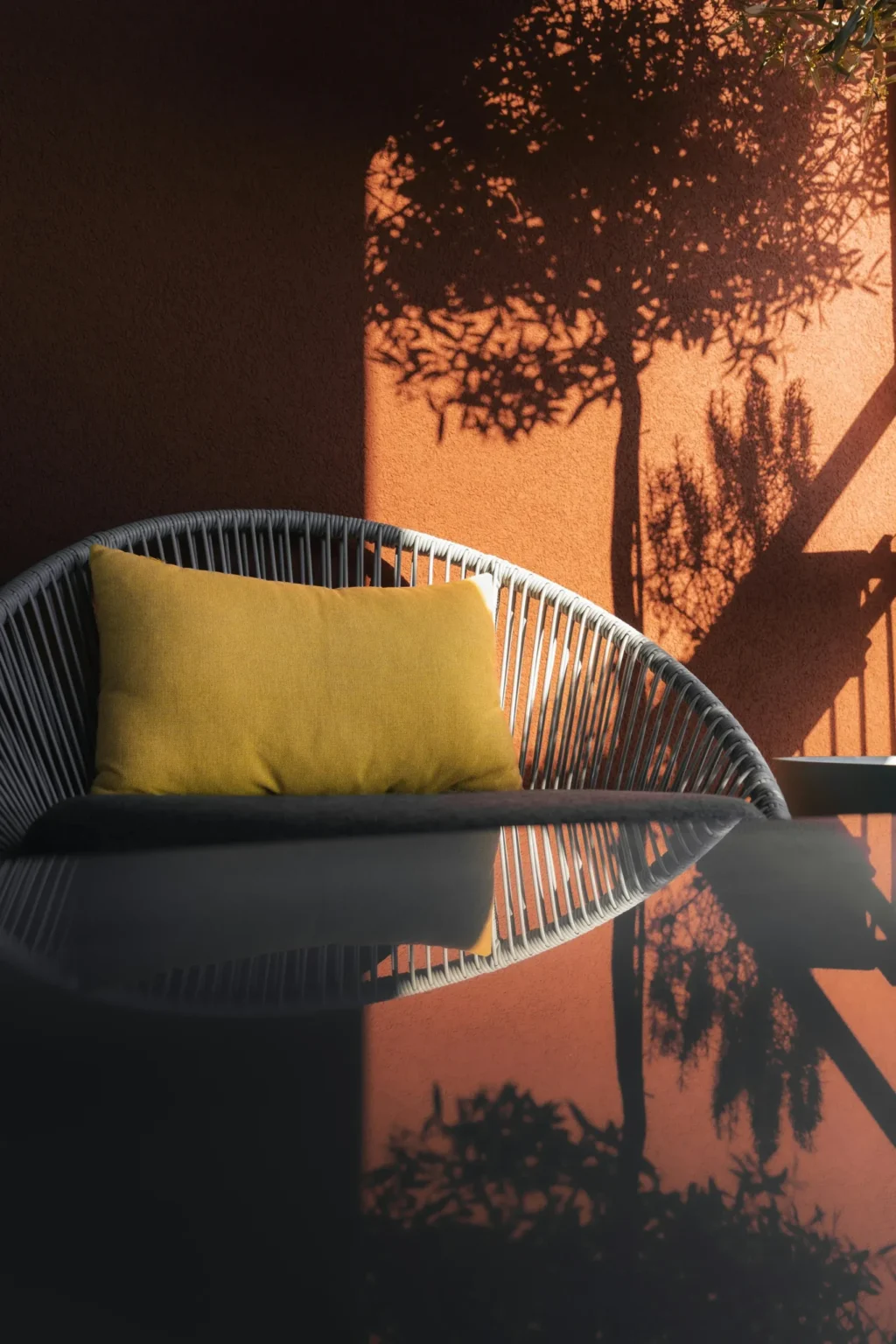 Luxury outdoor patio furniture with a grey woven chair and yellow cushion reflecting on a dark table, showcasing West Vancouver home improvement trends.