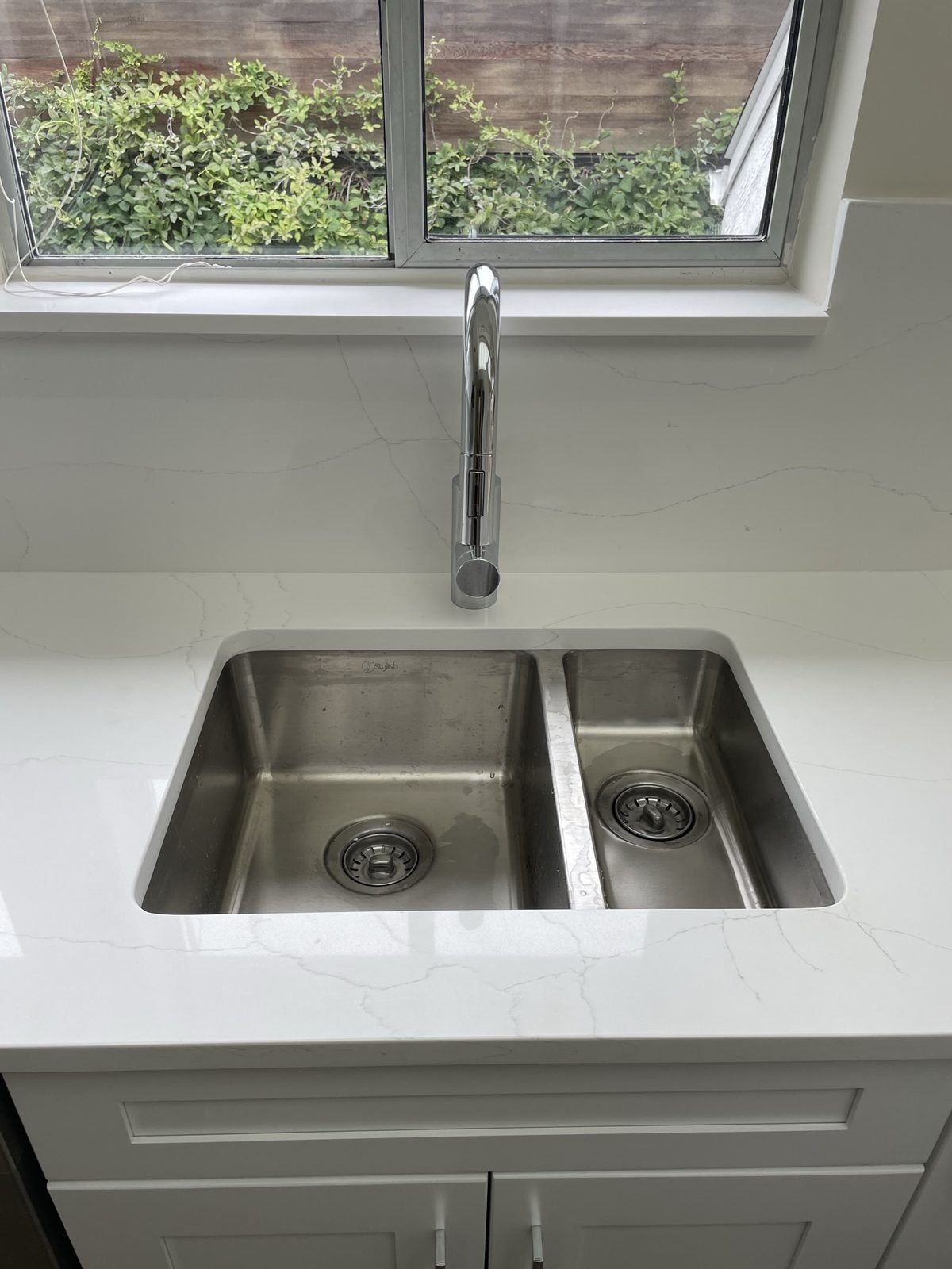 Stainless double undermount sink and pull-down faucet in white quartz in a Kitsilano condo kitchen