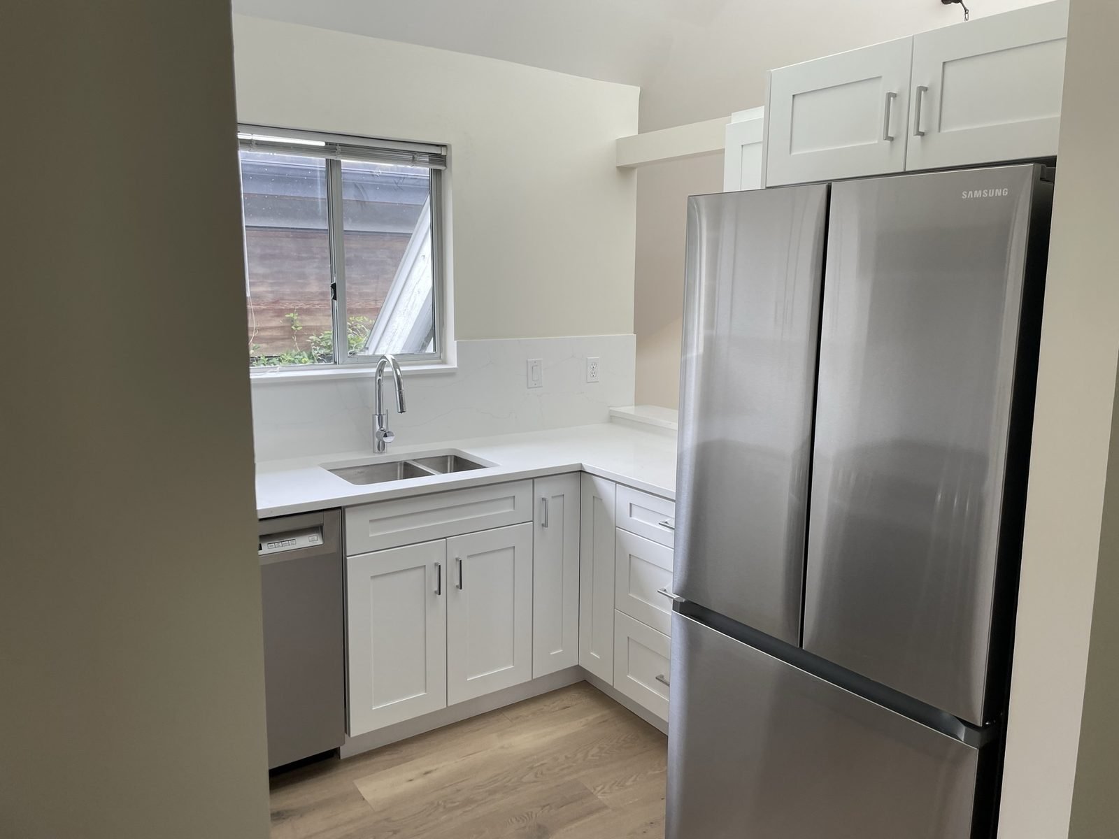 Stainless French-door fridge beside white shaker cabinets and quartz in a renovated Kitsilano condo kitchen