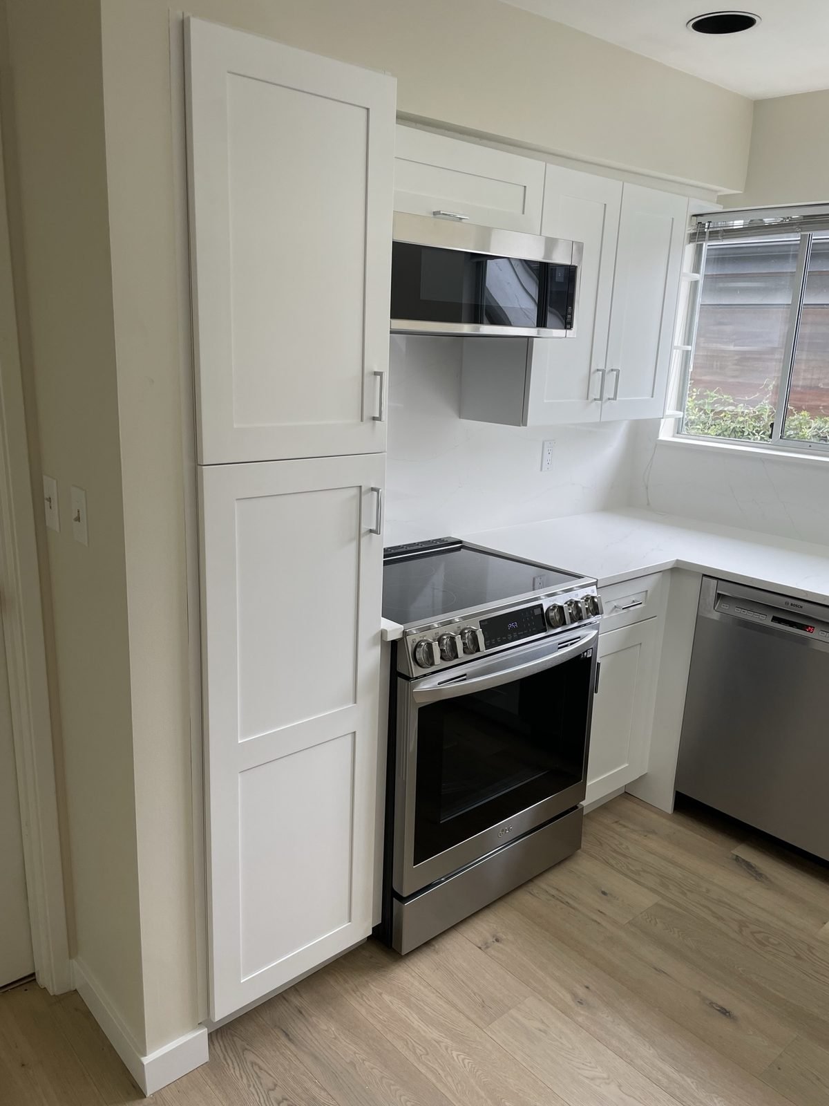 White shaker cabinets, tall pantry and a stainless electric range in a Kitsilano condo kitchen renovation