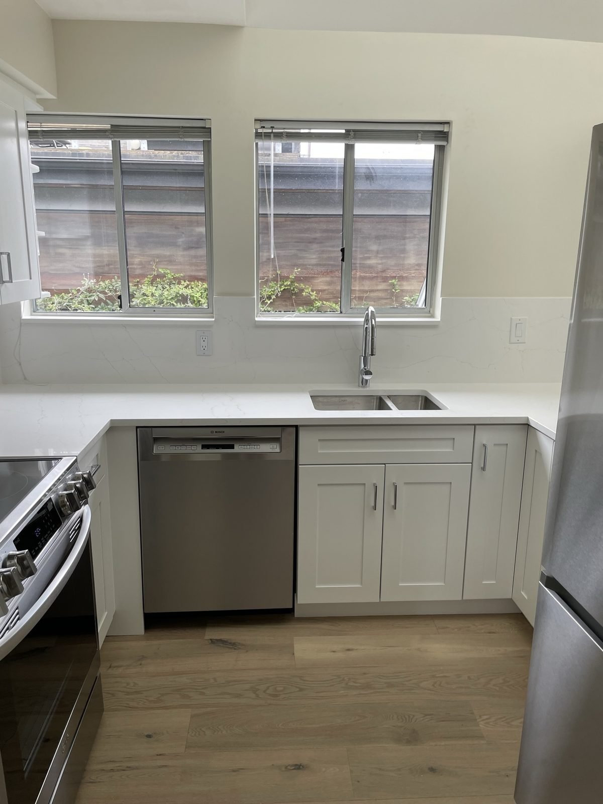 U-shaped kitchen with white shaker cabinets, quartz countertops and engineered hardwood in a Kitsilano condo