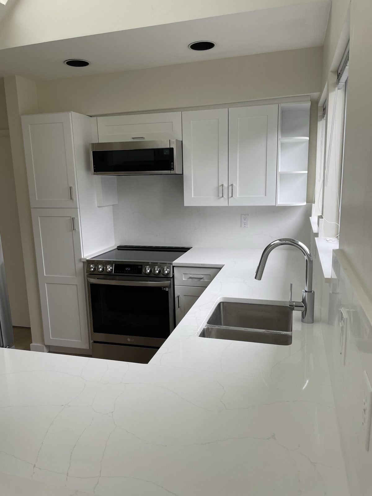 U-shaped white kitchen with quartz backsplash and over-the-range microwave in a Kitsilano condo