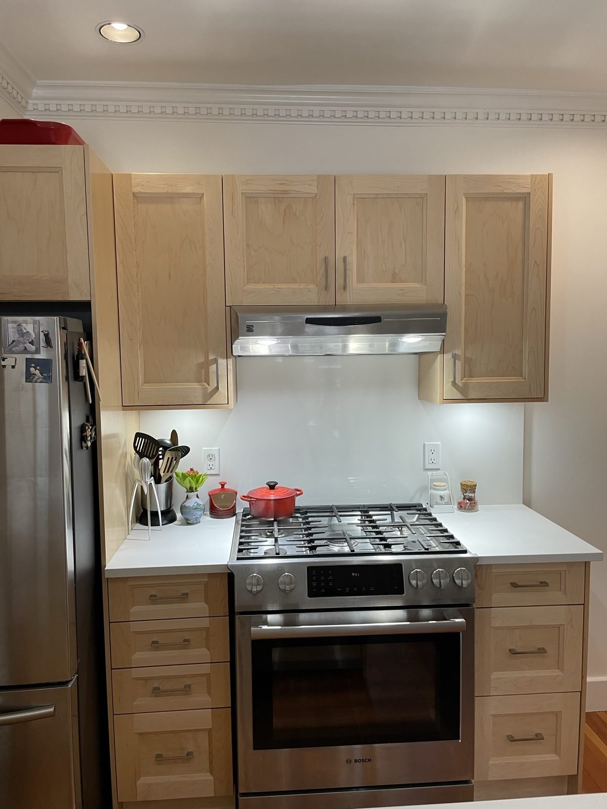 Gas range between maple shaker cabinets with white quartz and under-cabinet lighting in a Kitsilano kitchen
