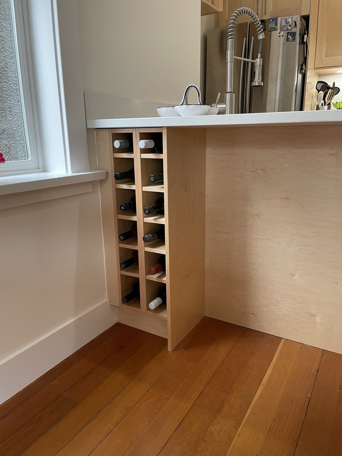 Built-in maple wine rack at the end of a quartz kitchen island in a Kitsilano renovation