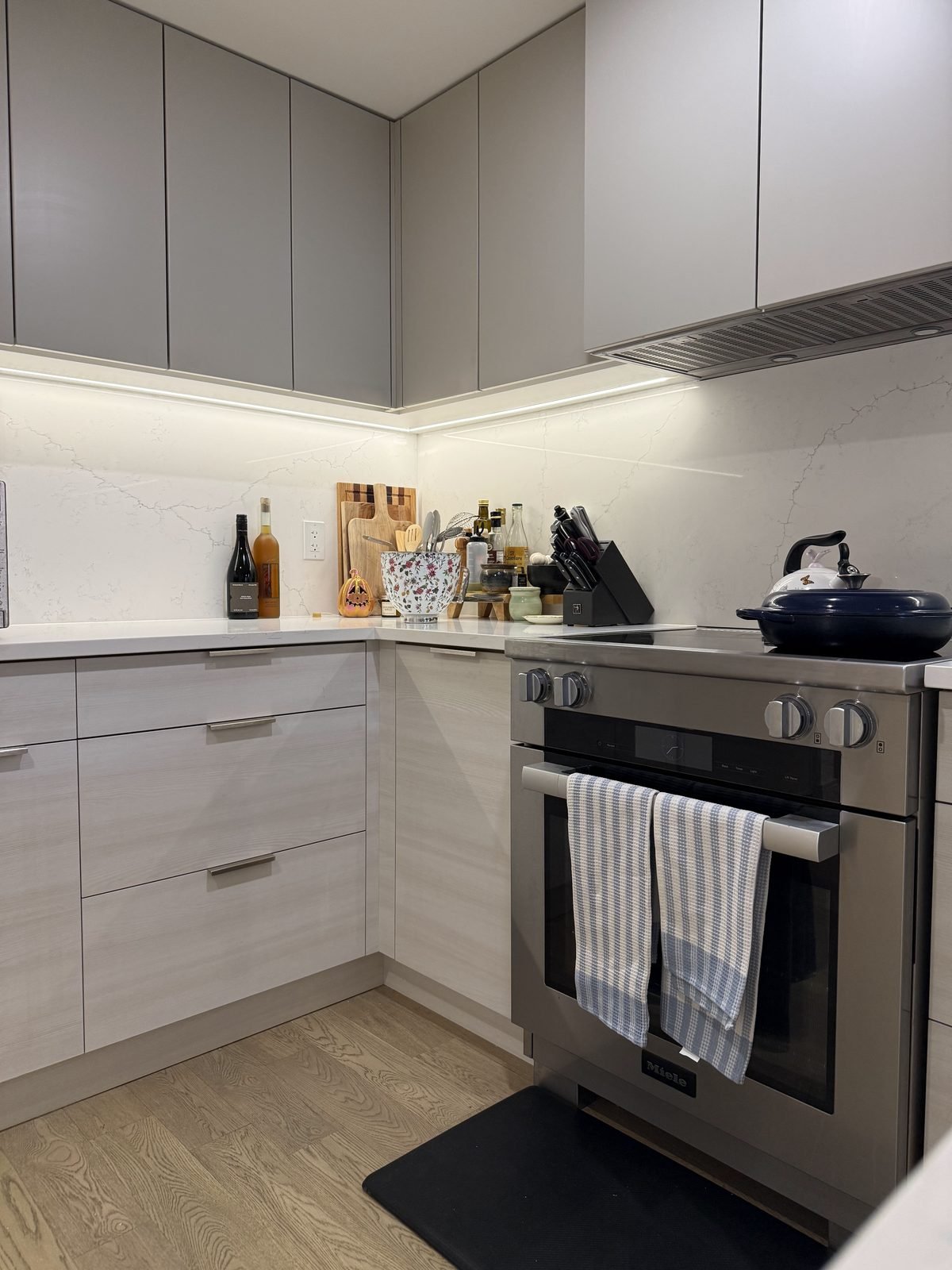 Range wall with white quartz counters, slab backsplash and under-cabinet LED lighting in a renovated North Vancouver kitchen