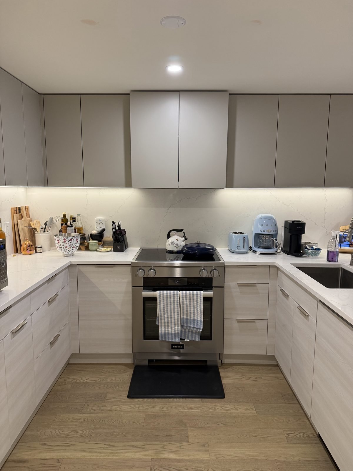Renovated U-shaped kitchen in Moodyville, North Vancouver with light woodgrain lower cabinets, white quartz countertops and a full-height slab backsplash