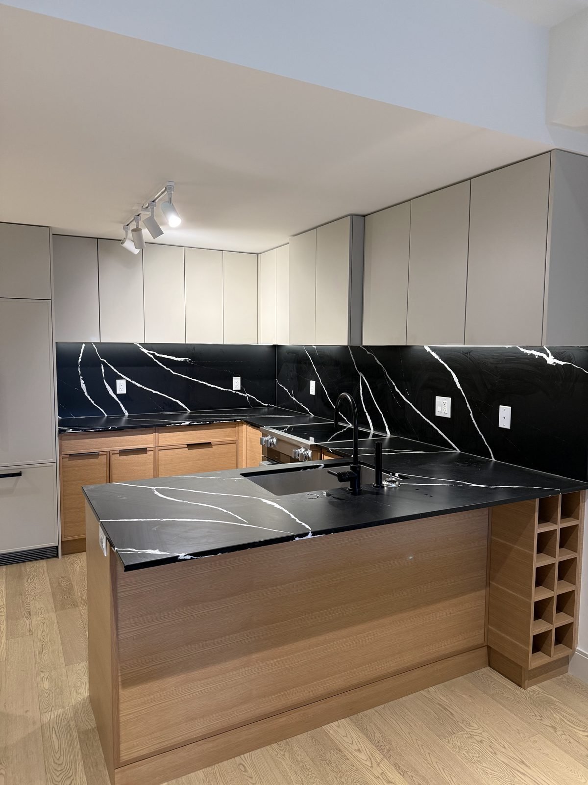 Before: oak lower cabinets, black quartz peninsula and track lighting in a Moodyville, North Vancouver kitchen