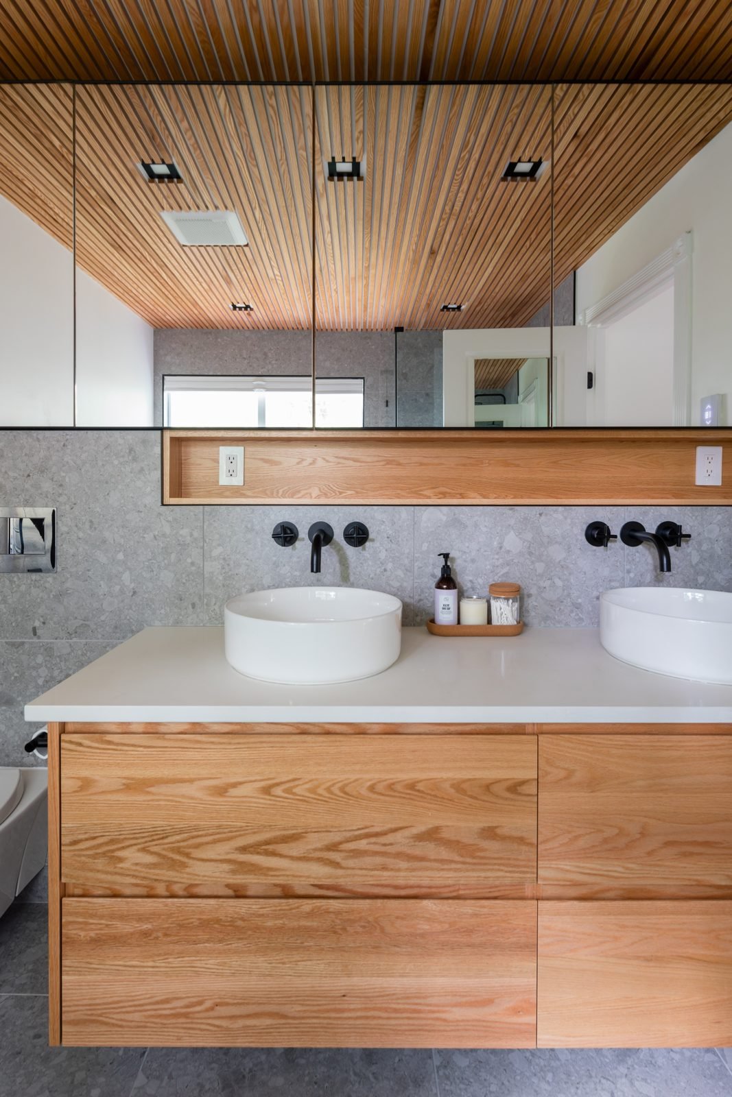 Floating wood double vanity with round vessel sinks and wall-mount black faucets in a North Vancouver ensuite