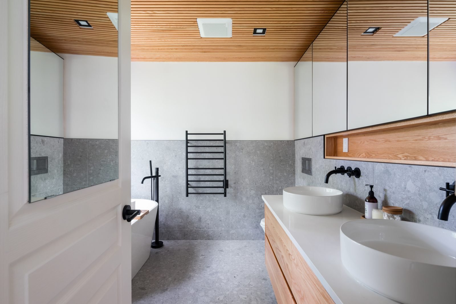 Mirrored medicine cabinets, wood slat ceiling and heated towel rail in a renovated North Vancouver ensuite