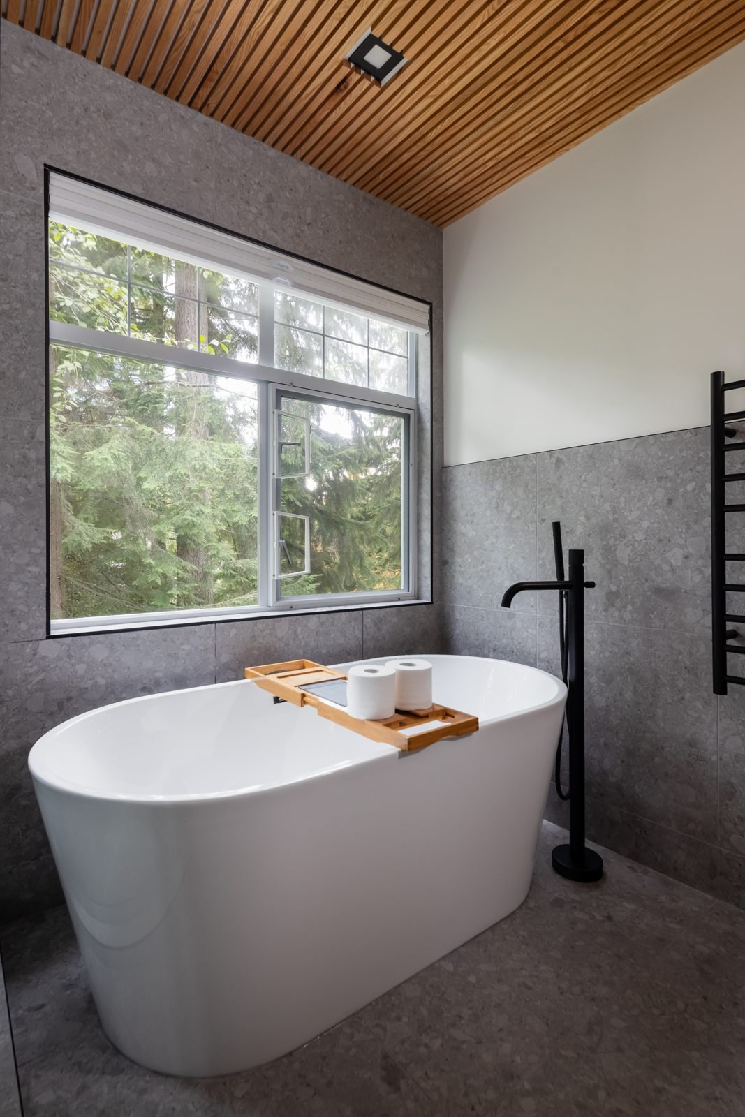 Freestanding soaker tub under a forest-view window in a North Vancouver ensuite renovation