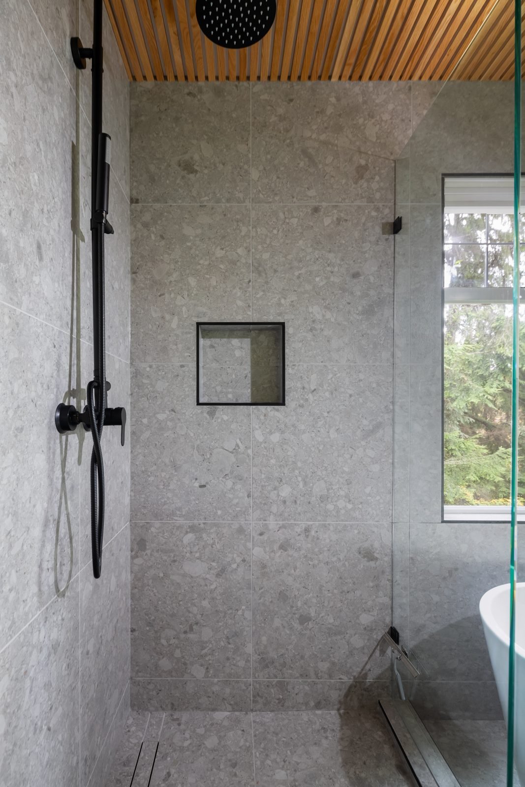 Walk-in shower with grey terrazzo-look tile, recessed niche and black rain shower in a North Vancouver ensuite