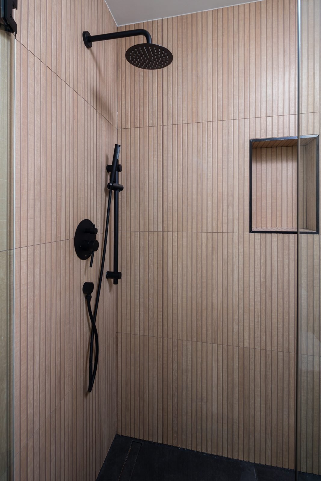 Tiled shower with fluted wall tile, recessed niche and black rain shower in a North Vancouver main bathroom