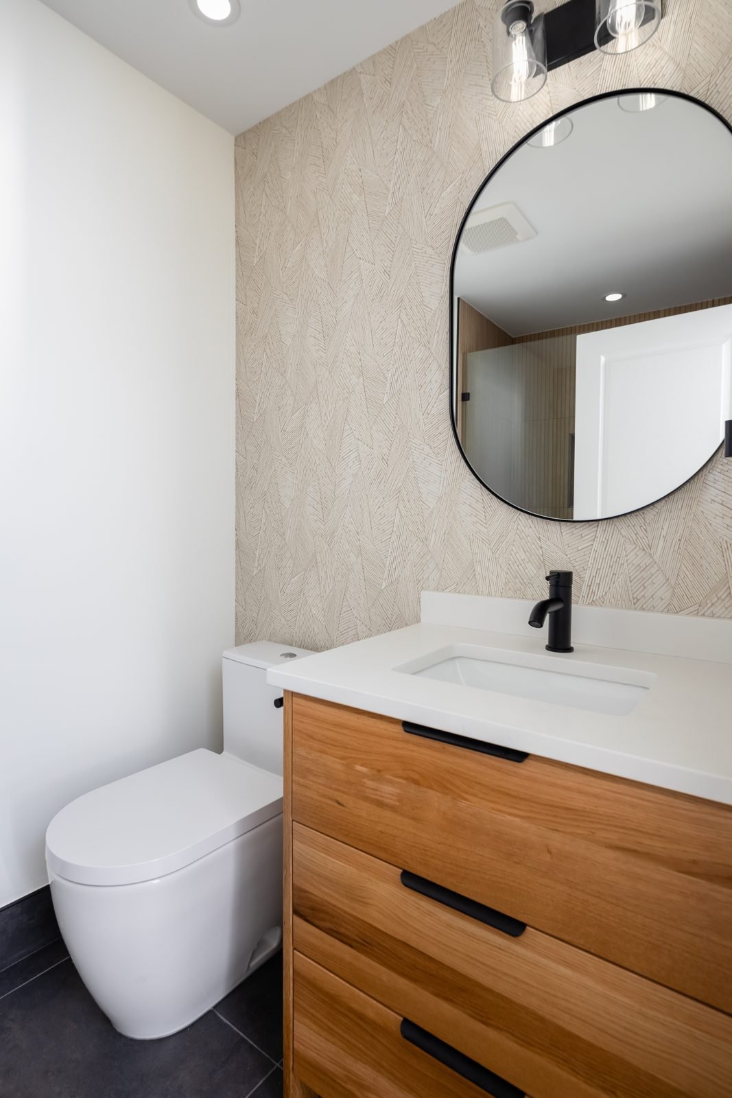 Wood vanity with quartz countertop, black faucet and oval mirror in a renovated North Vancouver main bathroom