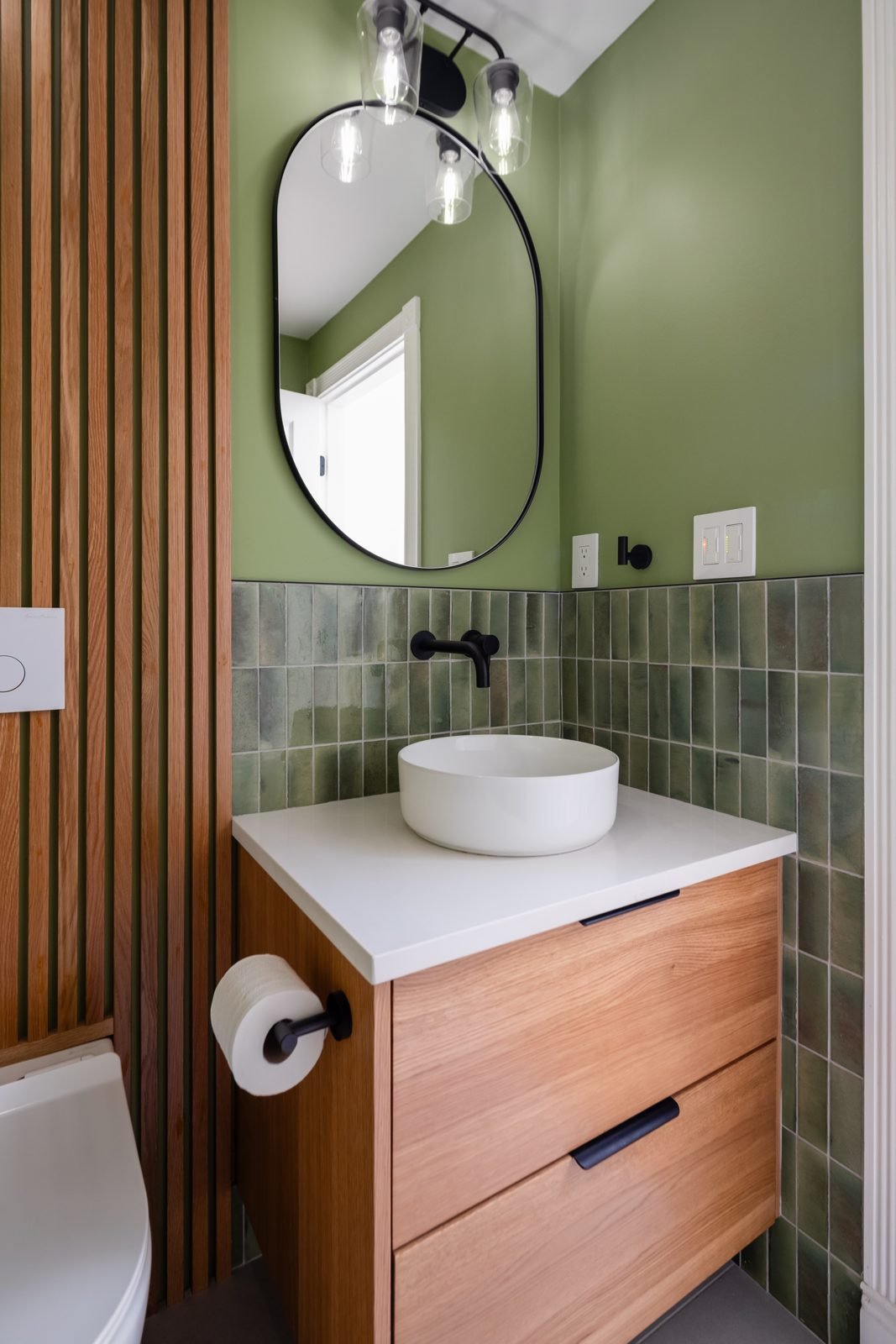 Floating wood vanity and wall-hung toilet in front of a wood slat wall in a North Vancouver powder room