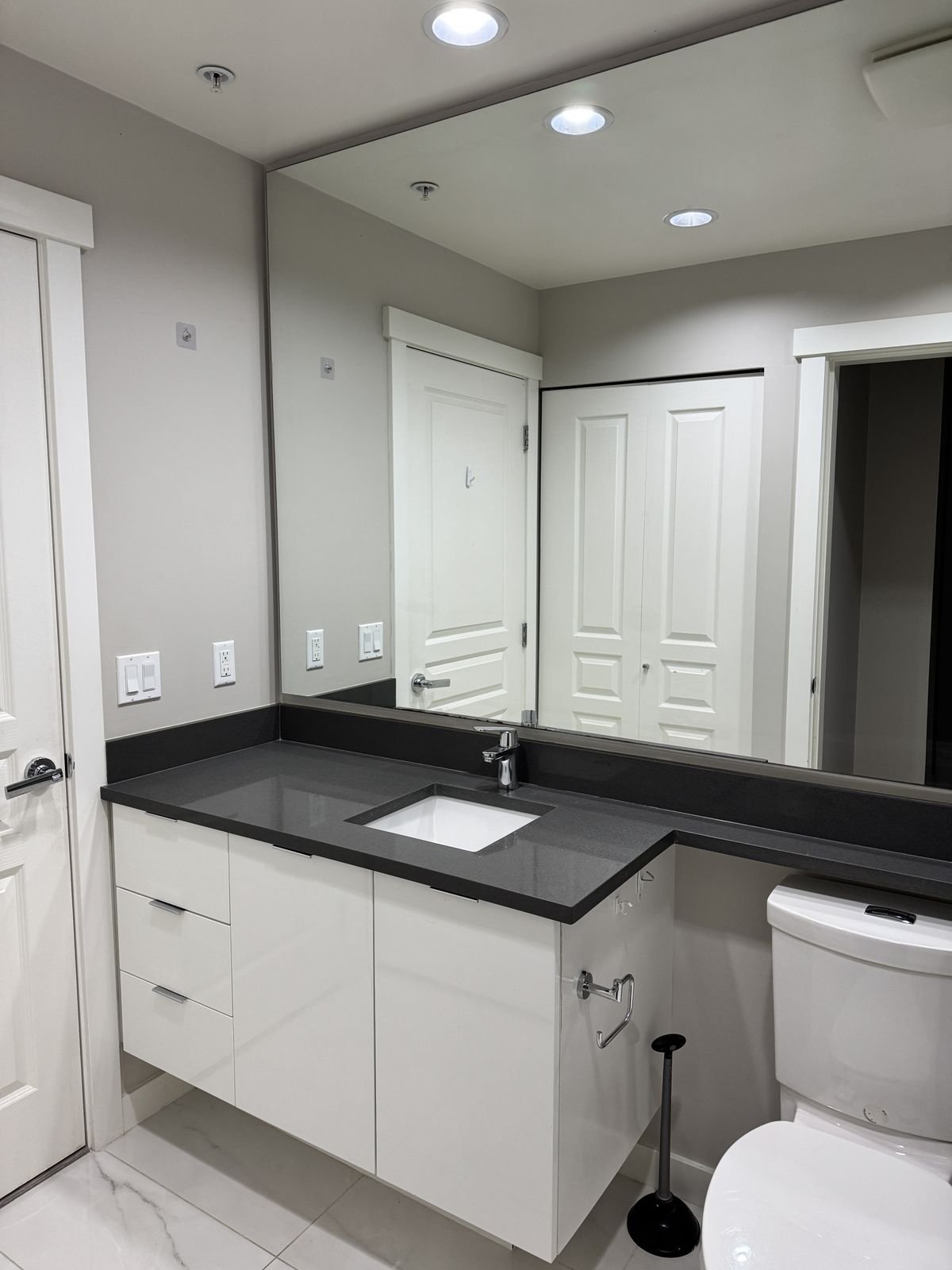 Before: Richmond condo bathroom with a white vanity, black countertop and wall-to-wall mirror