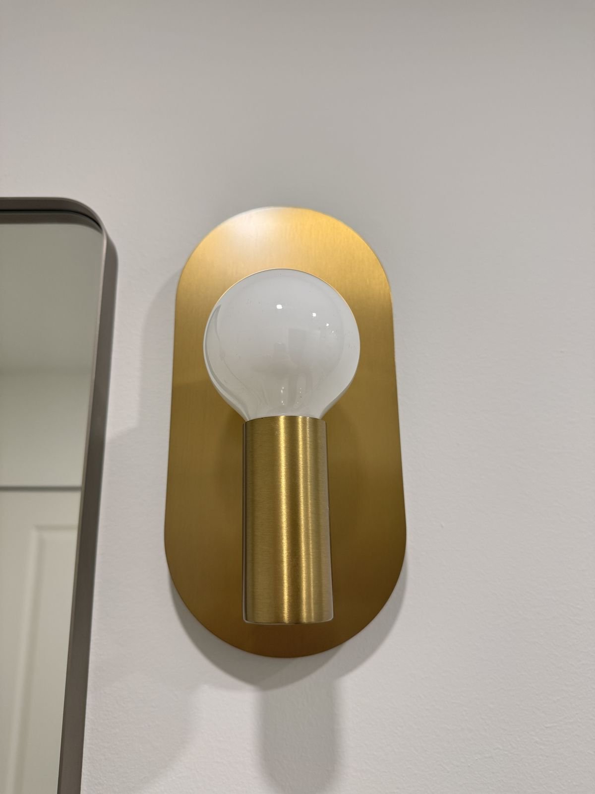Brass wall sconce with a globe bulb beside a black-framed mirror in a renovated Richmond condo bathroom