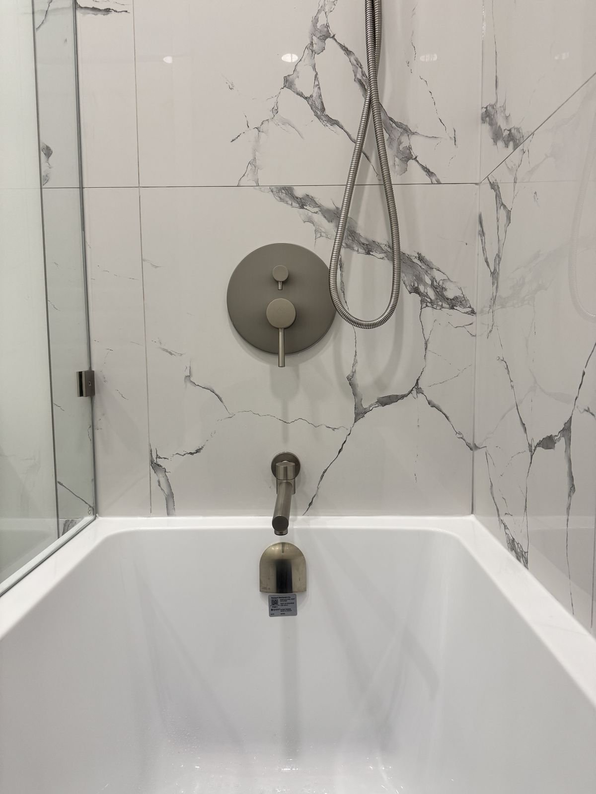 Brushed nickel tub valve, spout and hand shower on marble-look porcelain tile in a Richmond condo bathroom