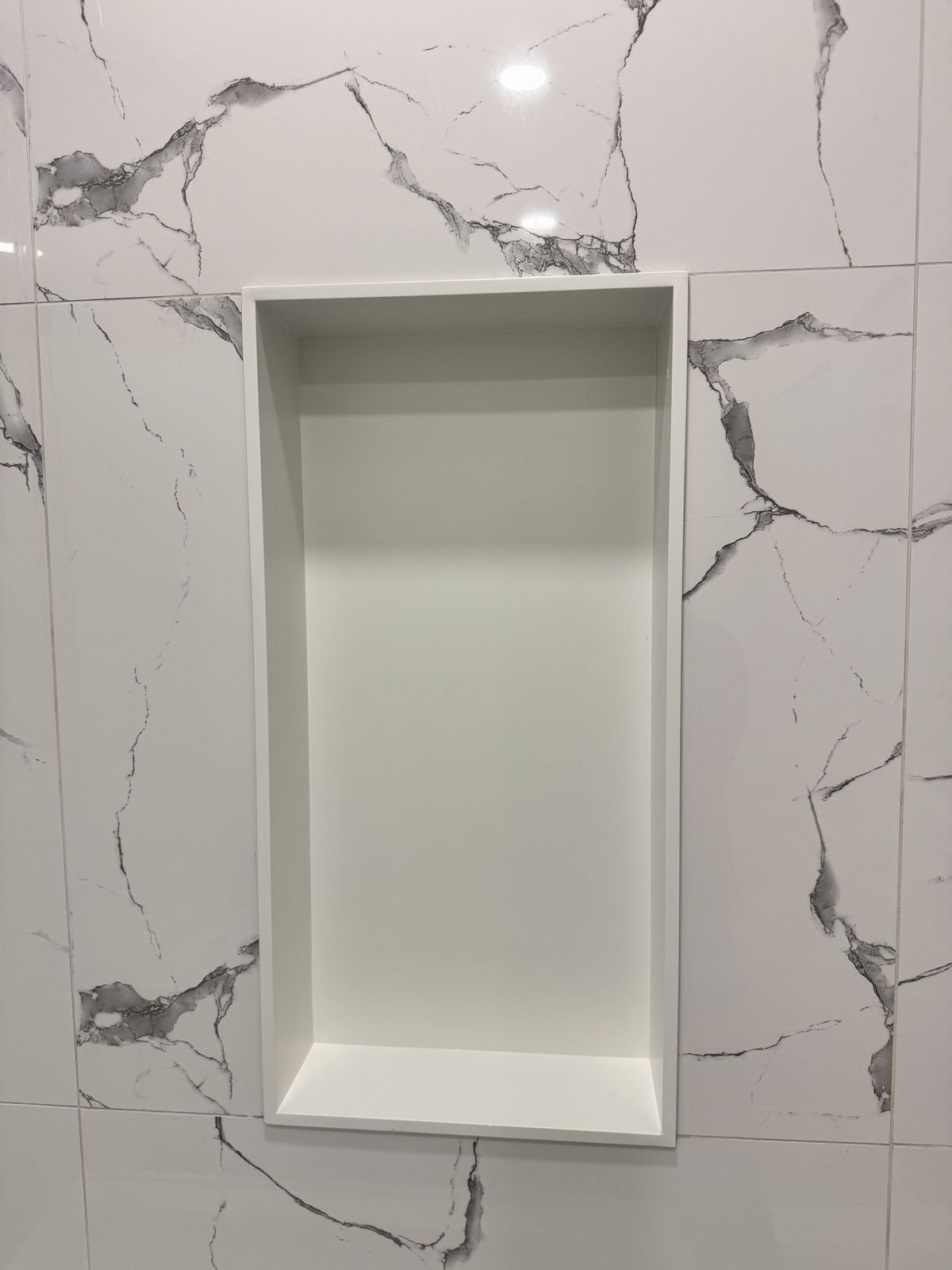 Recessed shower niche set into marble-look porcelain tile in a Richmond condo bathroom renovation
