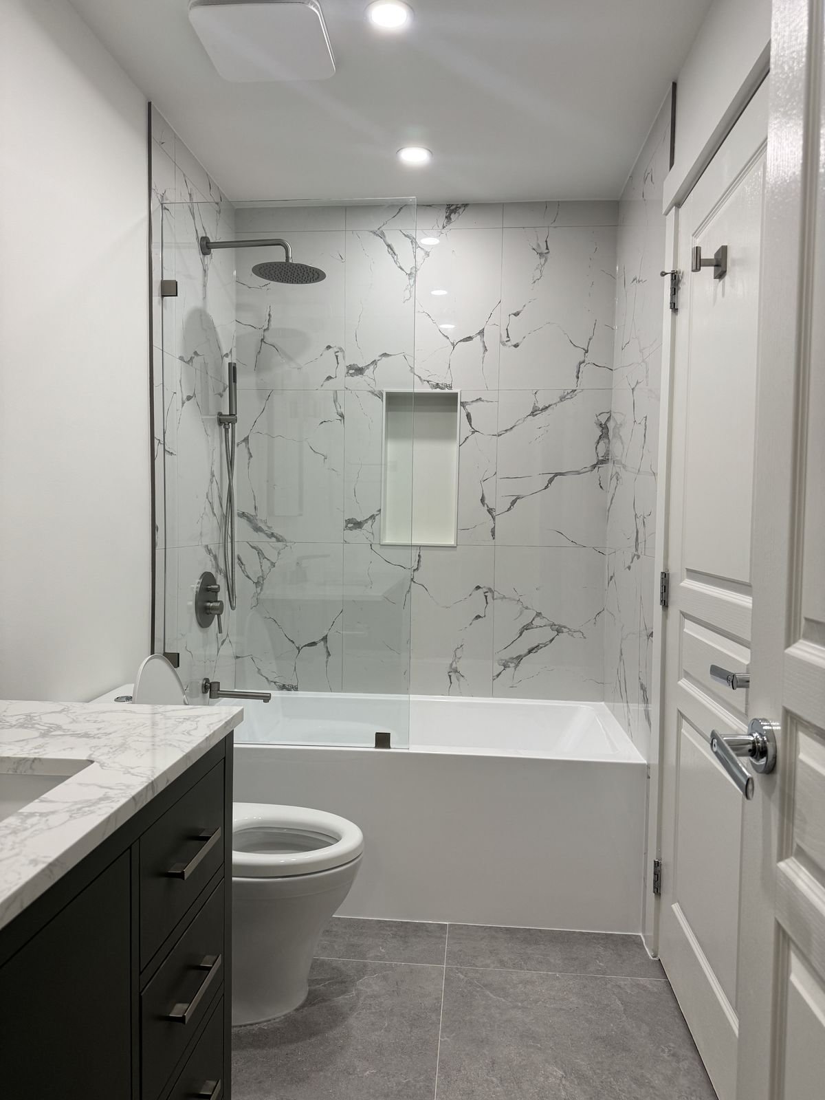 Renovated Richmond condo bathroom with a sage green vanity, marble-look tile and fixed glass tub panel