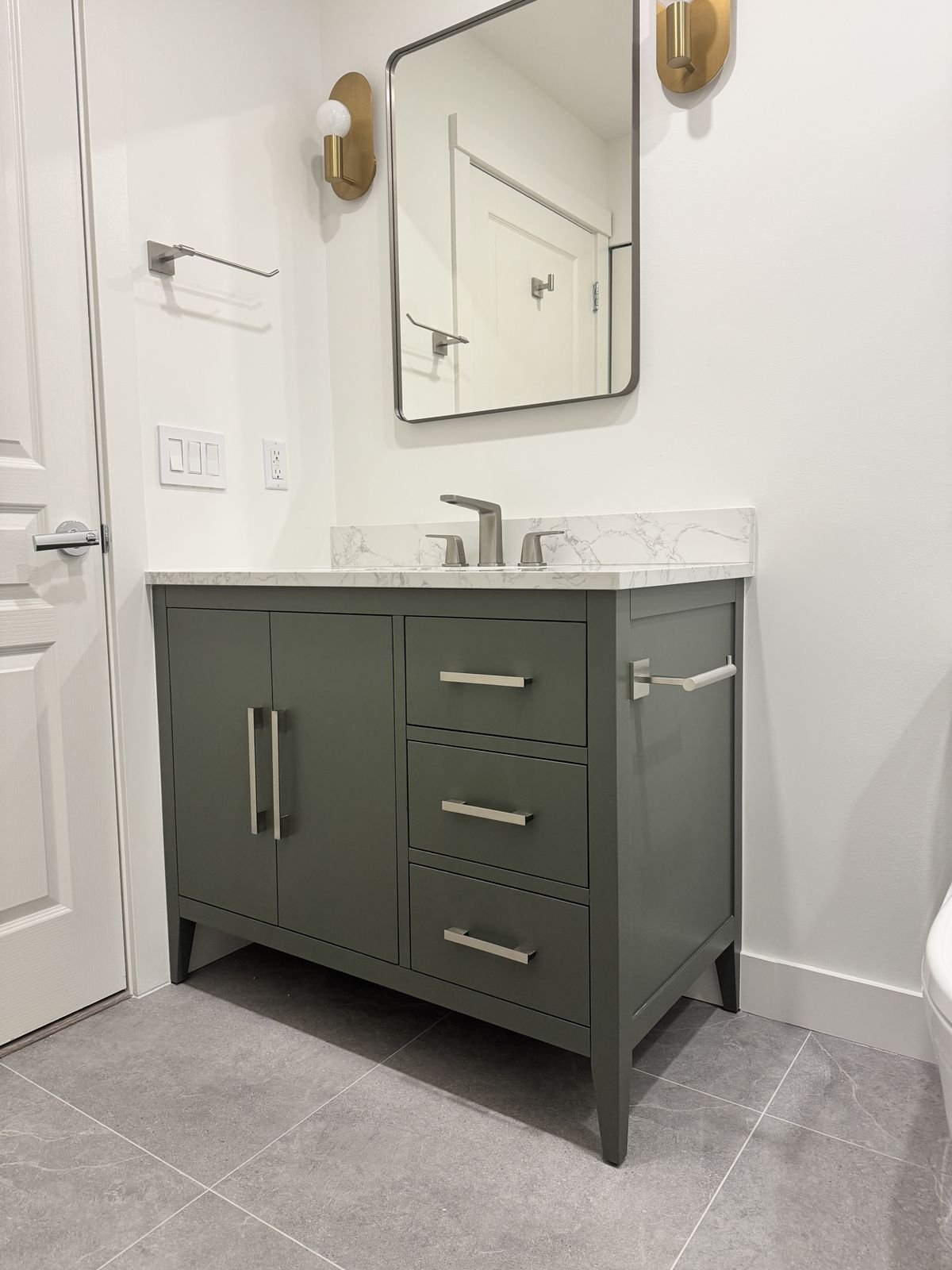 Sage green 36-inch vanity with a marble-look top, black-framed mirror and brass sconces in a Richmond condo