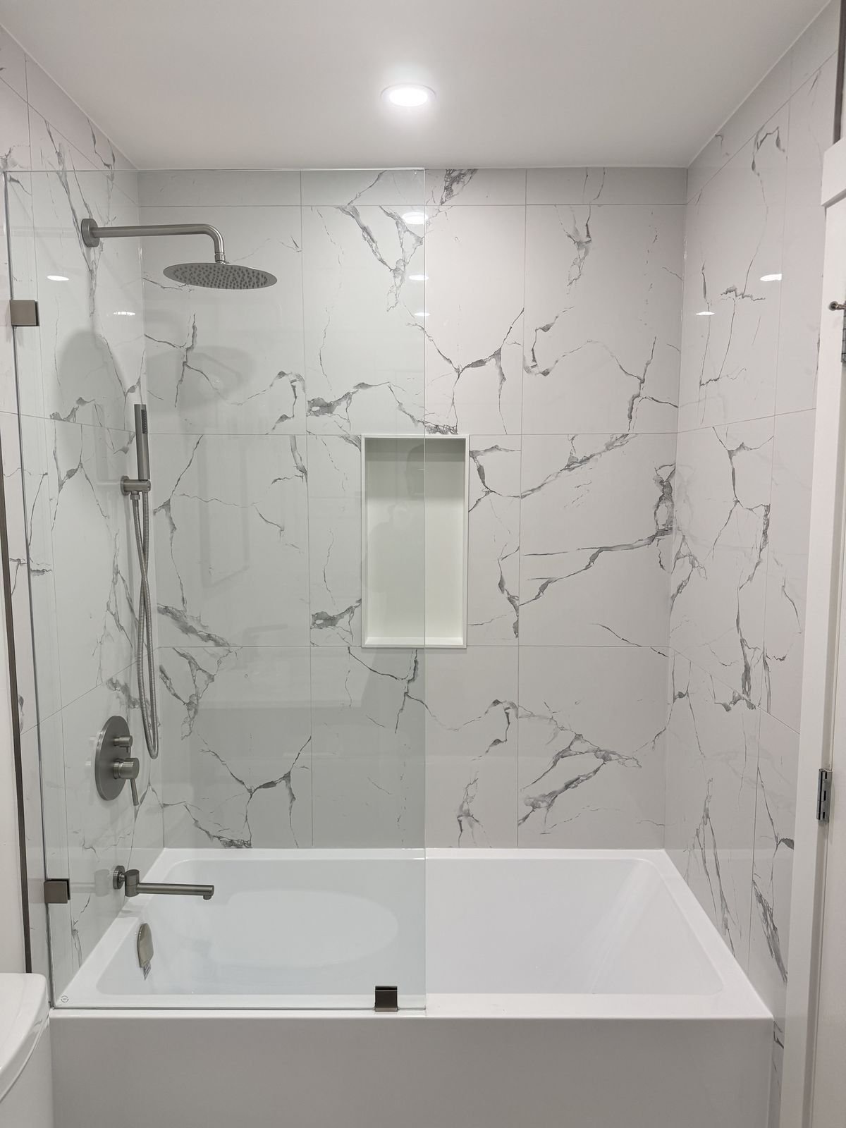 New bathtub with a fixed glass panel, rain shower and marble-look porcelain tile in a Richmond condo bathroom