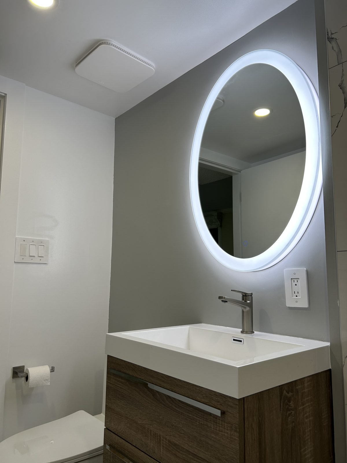 Wall-hung vanity and backlit oval mirror in a new accessible ground-floor bathroom in Shaughnessy