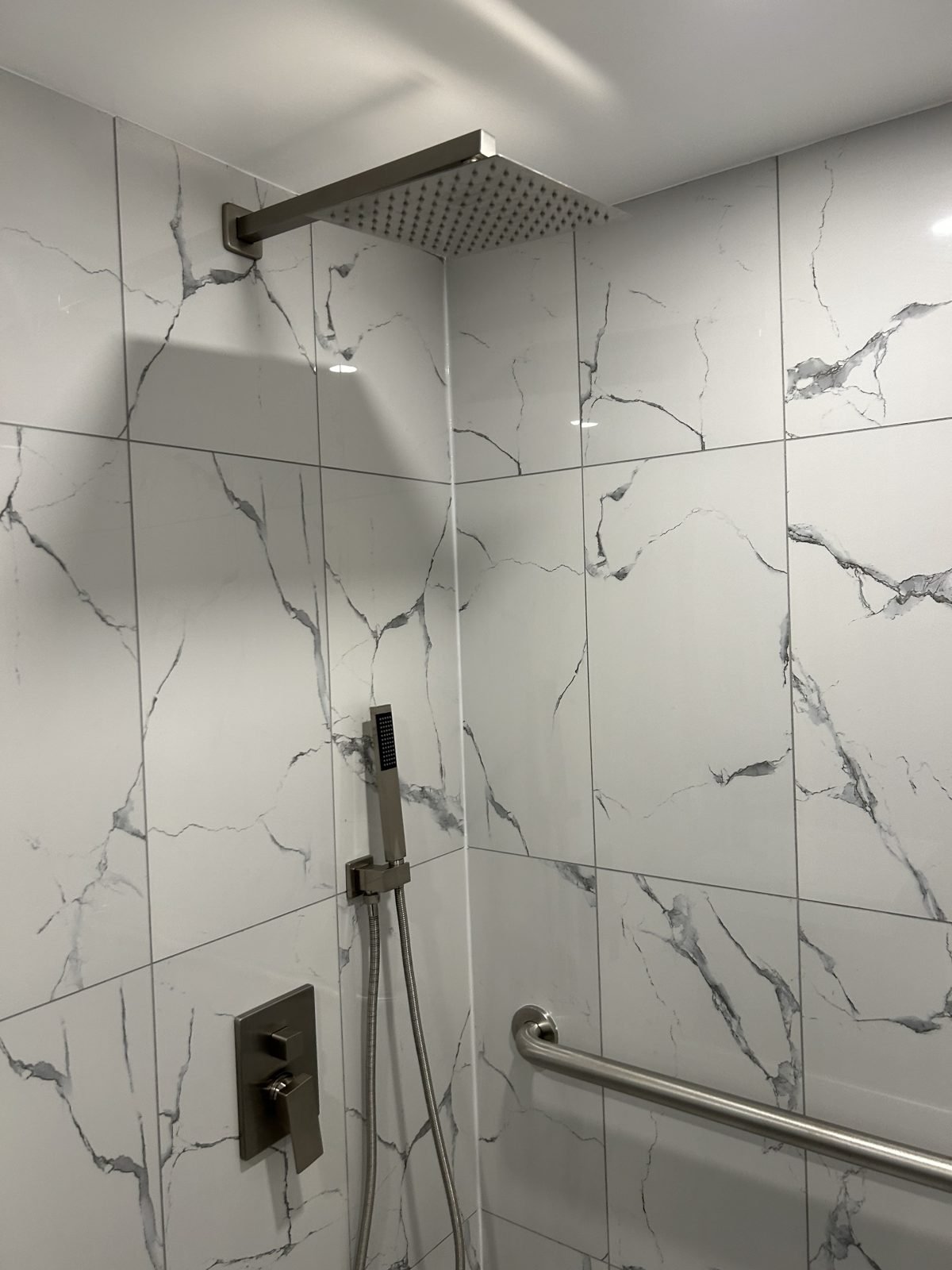 Hand shower on a slide bar beside a stainless grab bar in an accessible Shaughnessy shower