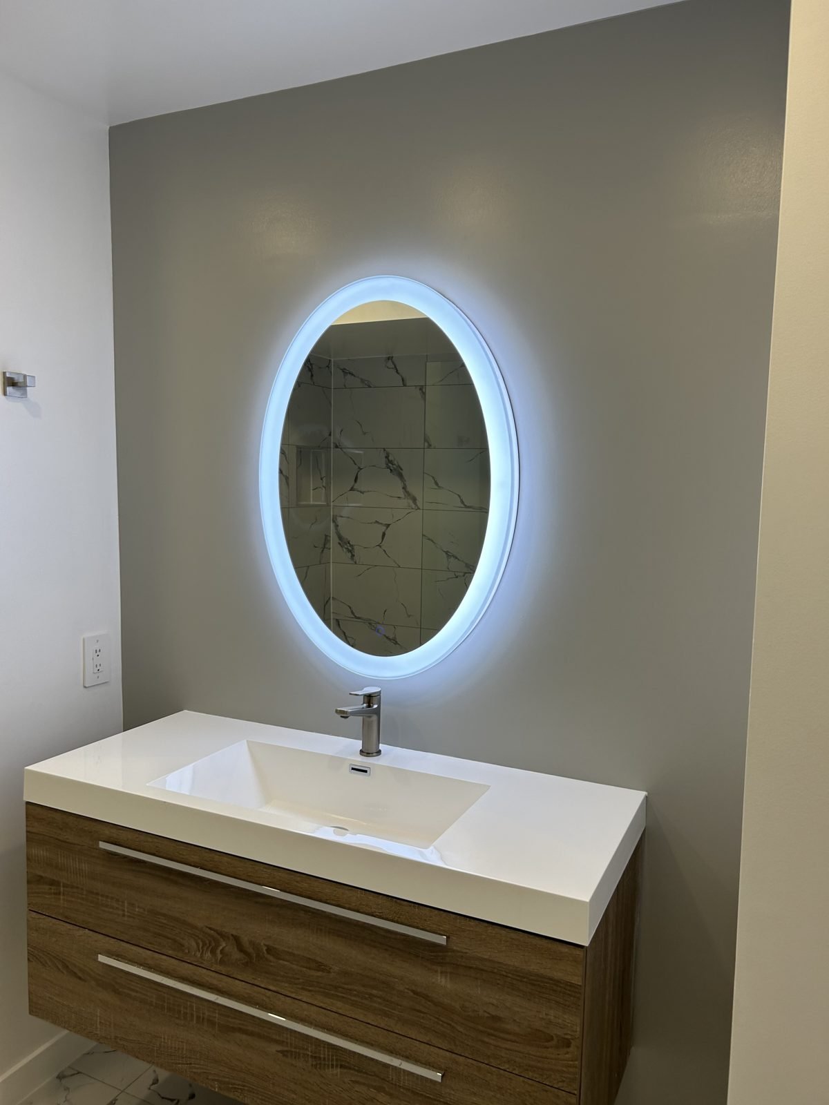 Wide floating wood-look vanity and backlit oval LED mirror on a grey accent wall in a Shaughnessy main bathroom