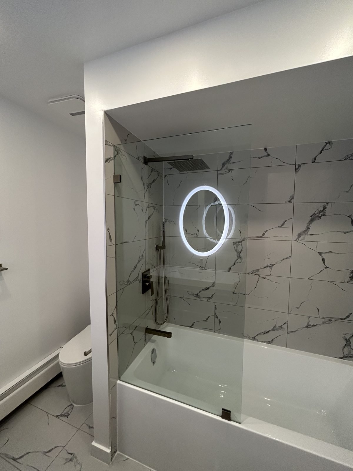 Renovated Shaughnessy main bathroom with a new tub, fixed glass panel and marble-look wall tile