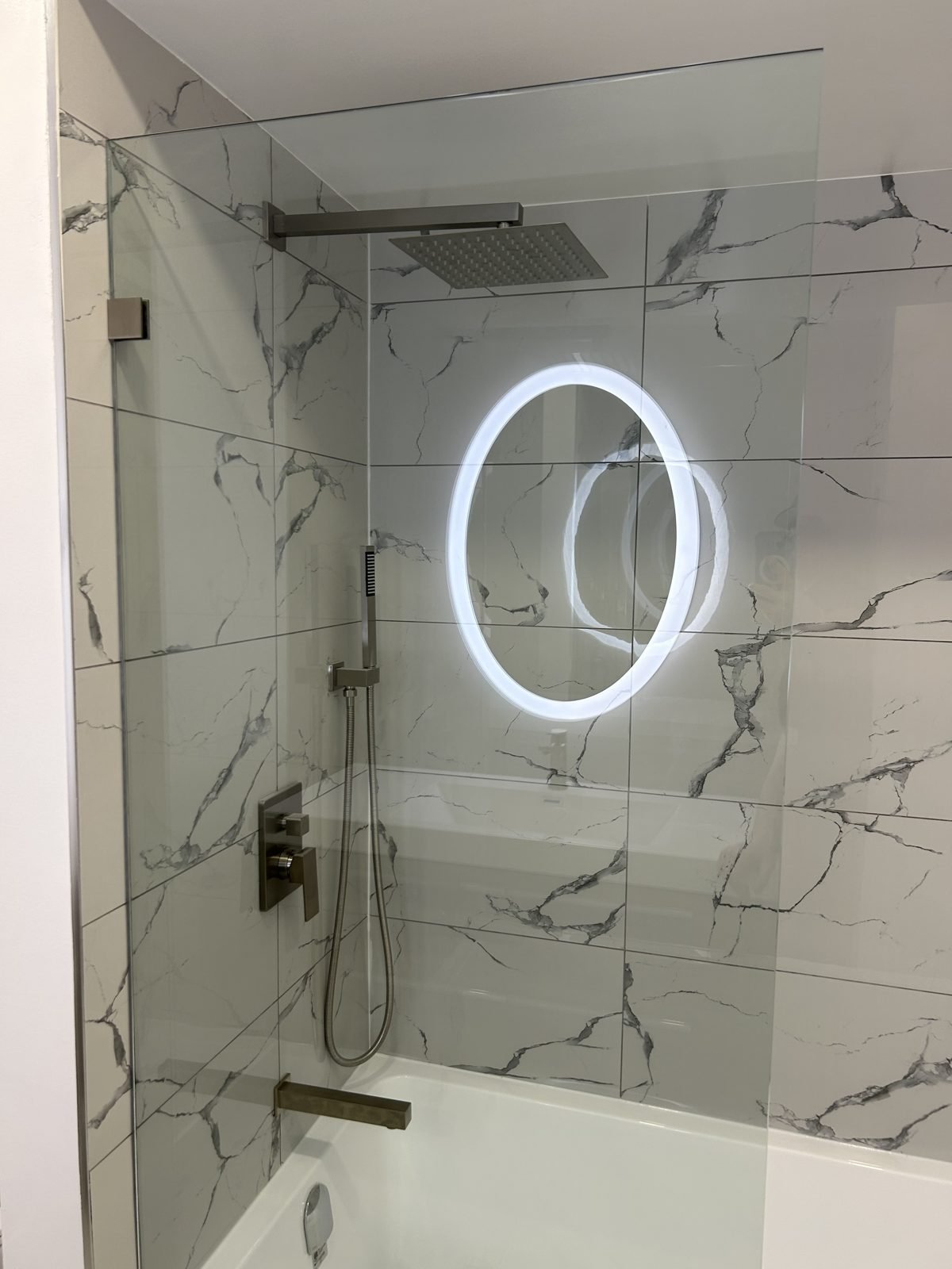Tub and shower combination with marble-look tile, rain head and glass panel in a renovated Shaughnessy bathroom