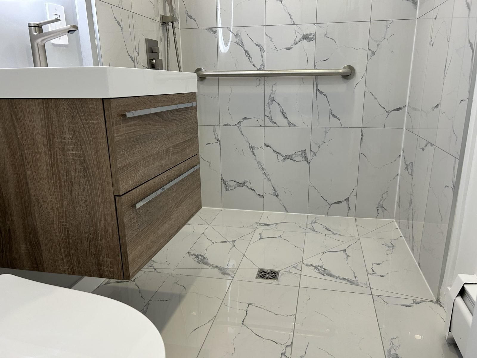Zero-threshold shower floor sloped to a drain, with continuous marble-look tile, in a Shaughnessy accessible bathroom