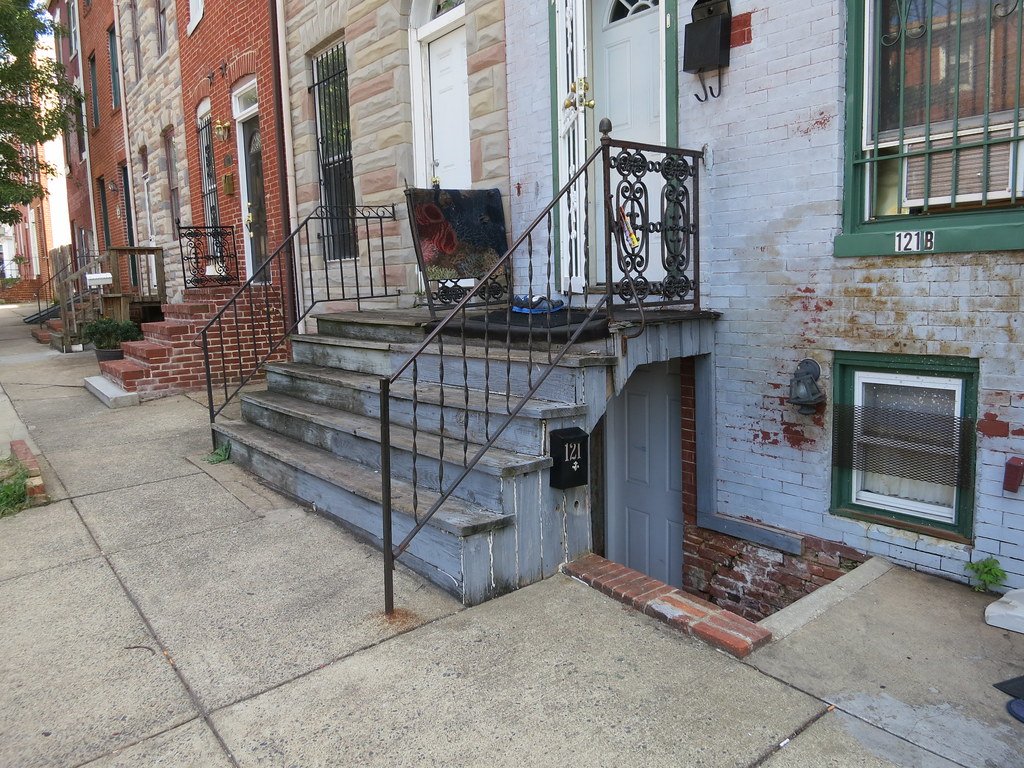 Exterior stairs with a railing leading down to a basement suite door beside the main entrance