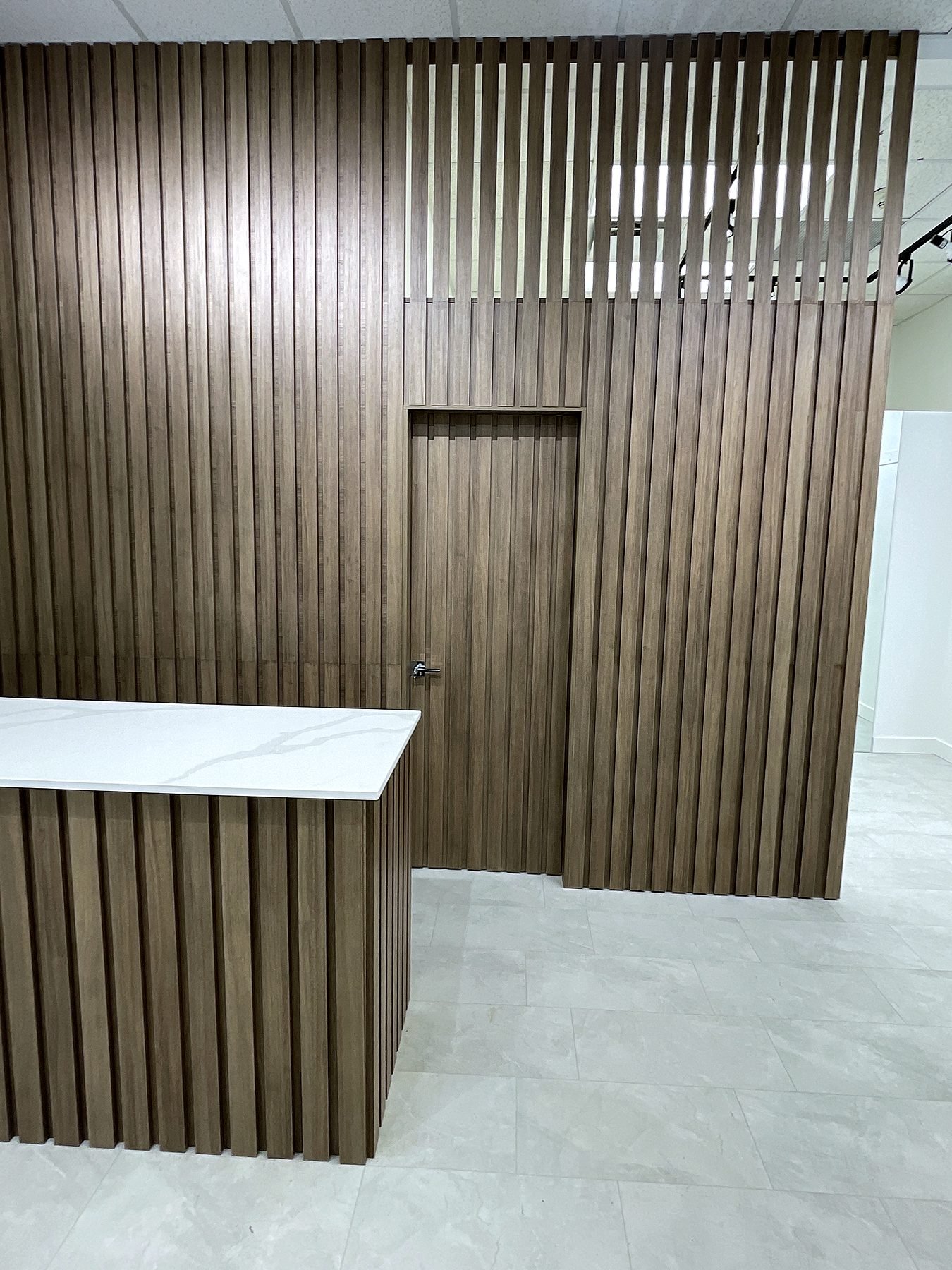 Cash desk clad in wood slats with a white quartz countertop in front of the slat feature wall