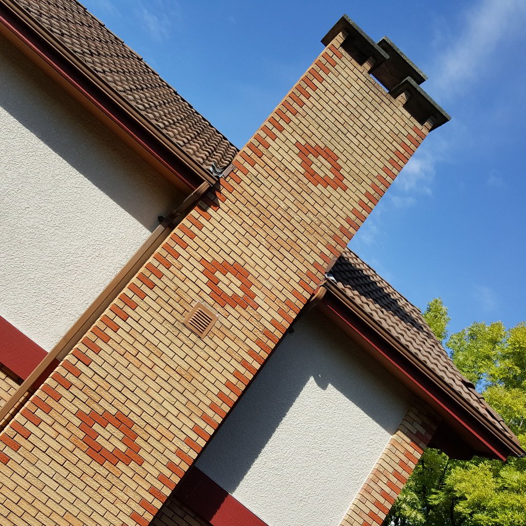 A Vancouver Special brick chimney with a diamond pattern against stucco walls and a tiled roof