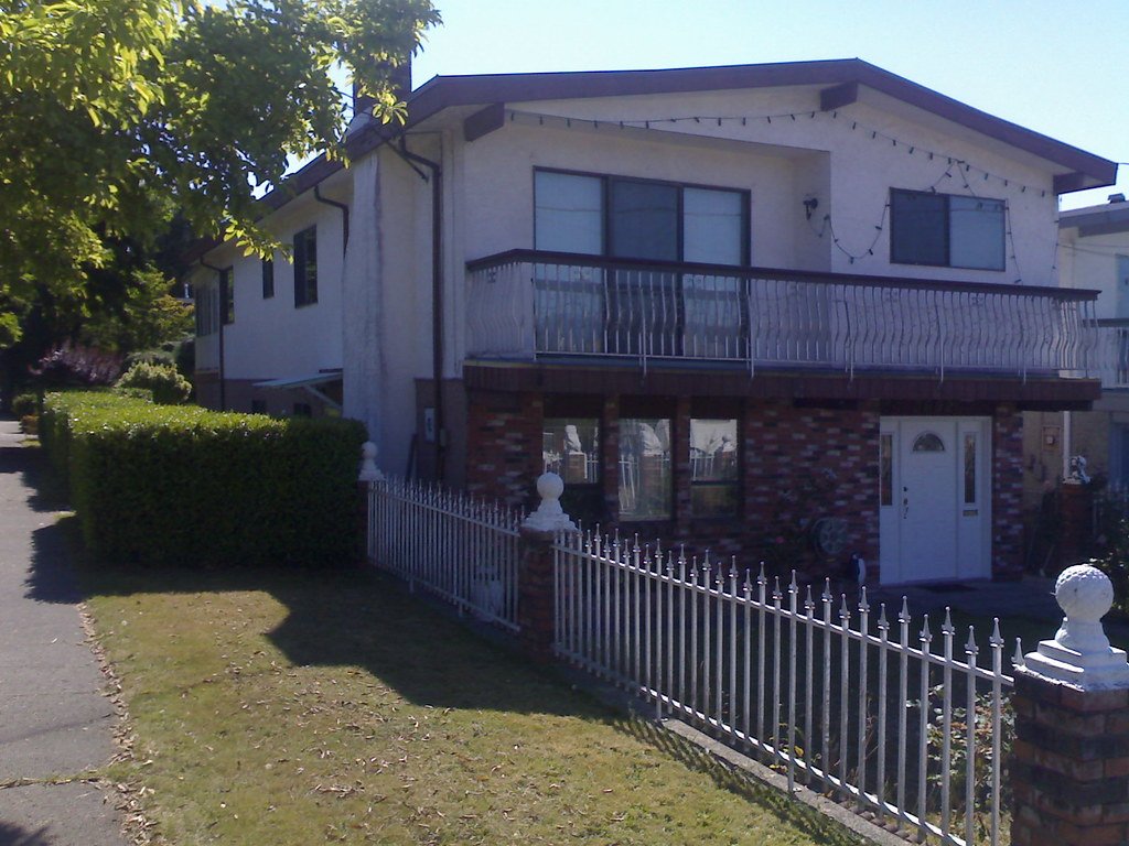 A Vancouver Special with deep roof overhangs, a second-floor balcony and a side-set front door