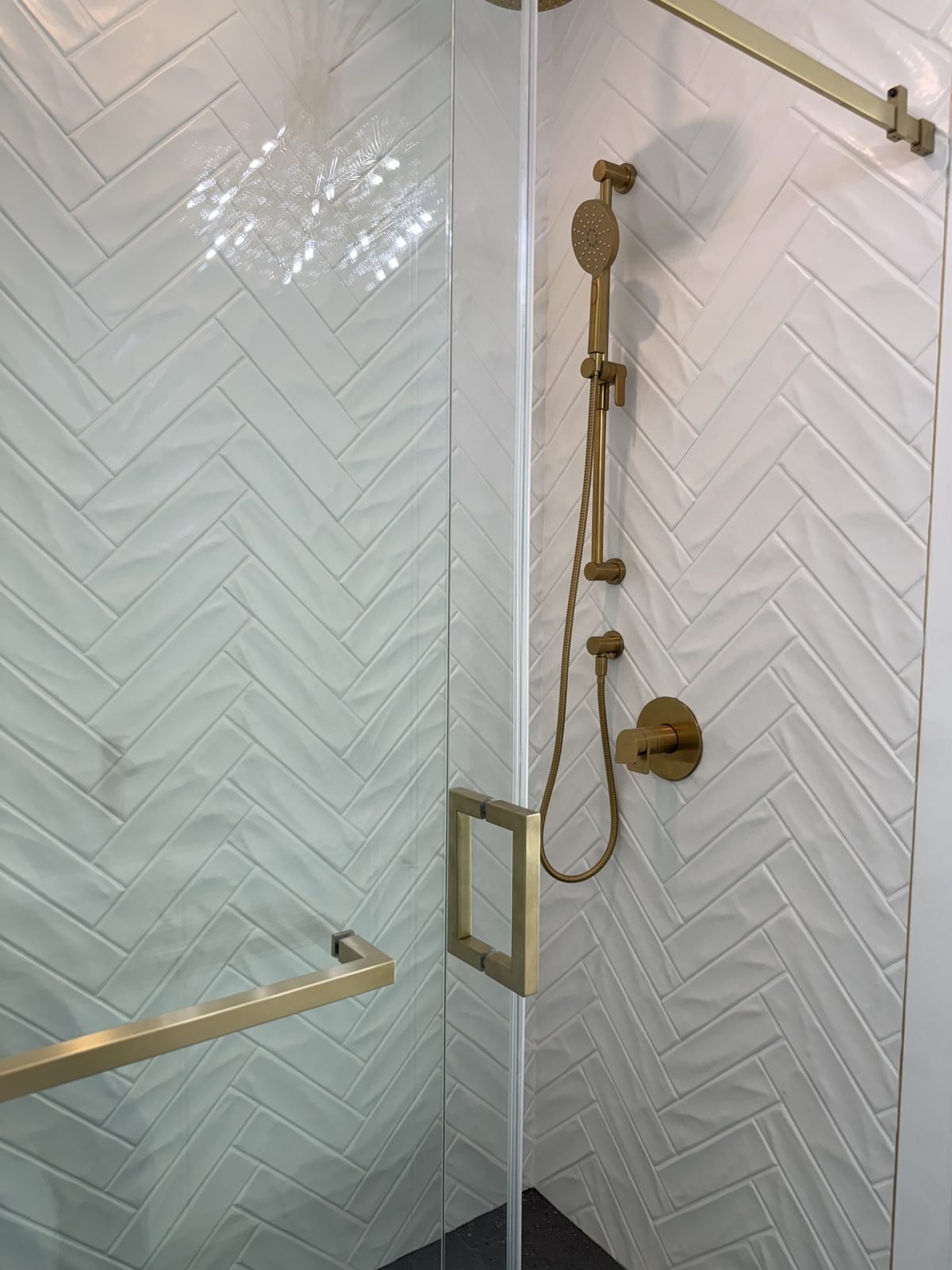 Brushed gold hand shower and trim on white herringbone tile in a West End condo ensuite
