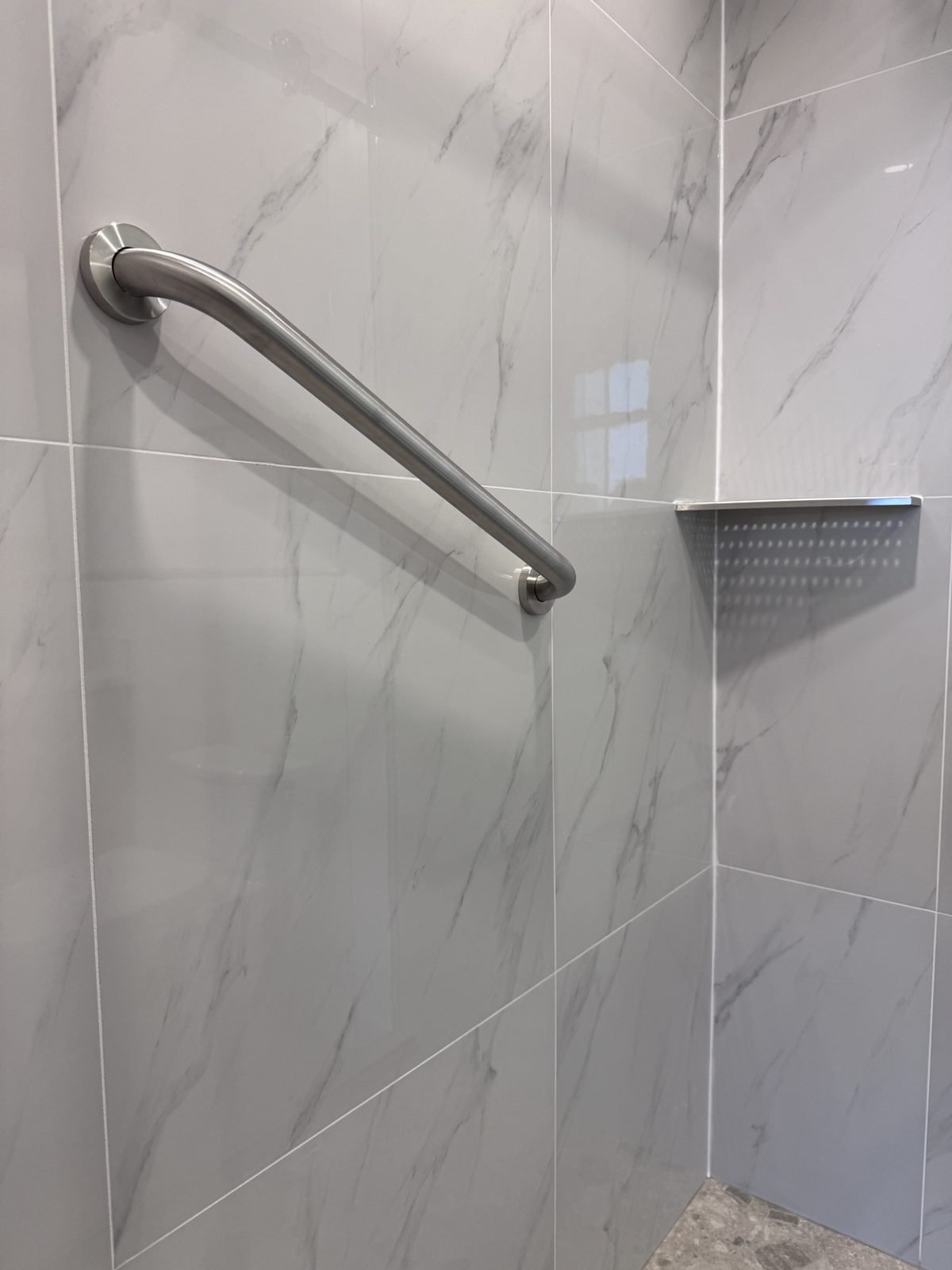 Shower grab bar and tiled corner shelf on marble-look porcelain in a West End condo ensuite