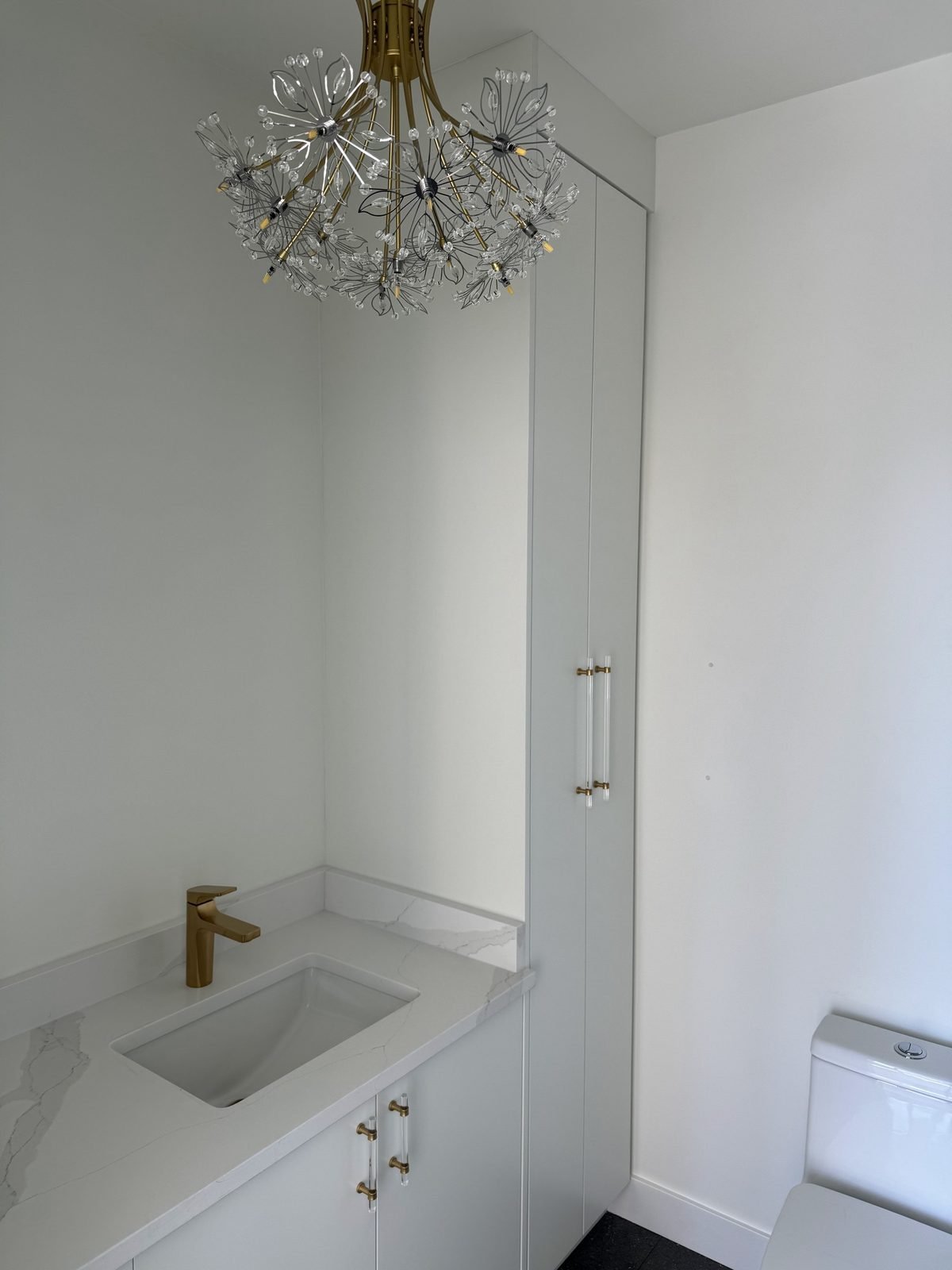 Custom white ensuite vanity with a tall pantry cabinet, brushed gold faucet and crystal chandelier in a West End condo