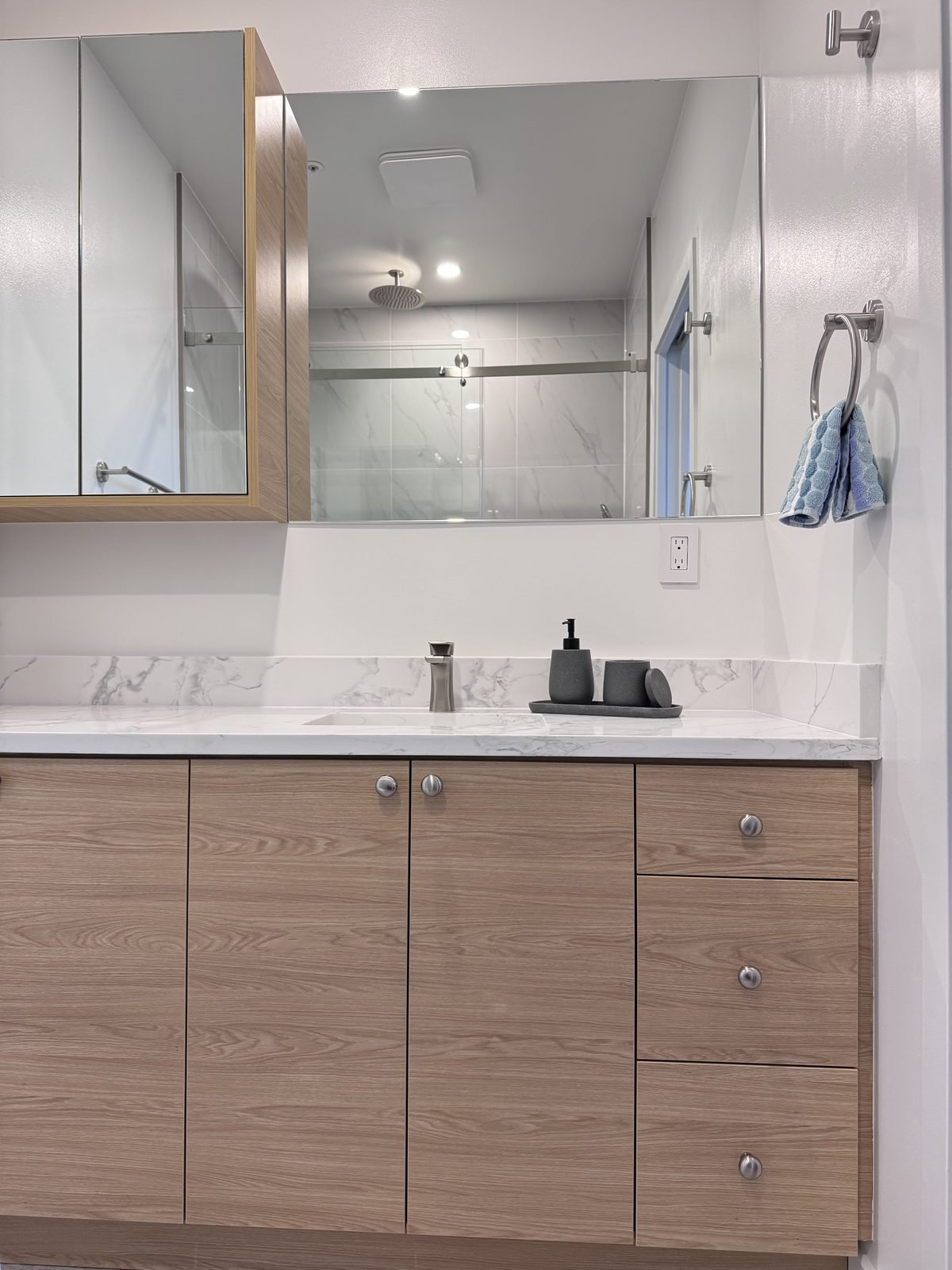 Wood-grain ensuite vanity with drawers, quartz top and undermount sink under a mirrored medicine cabinet in a West End condo