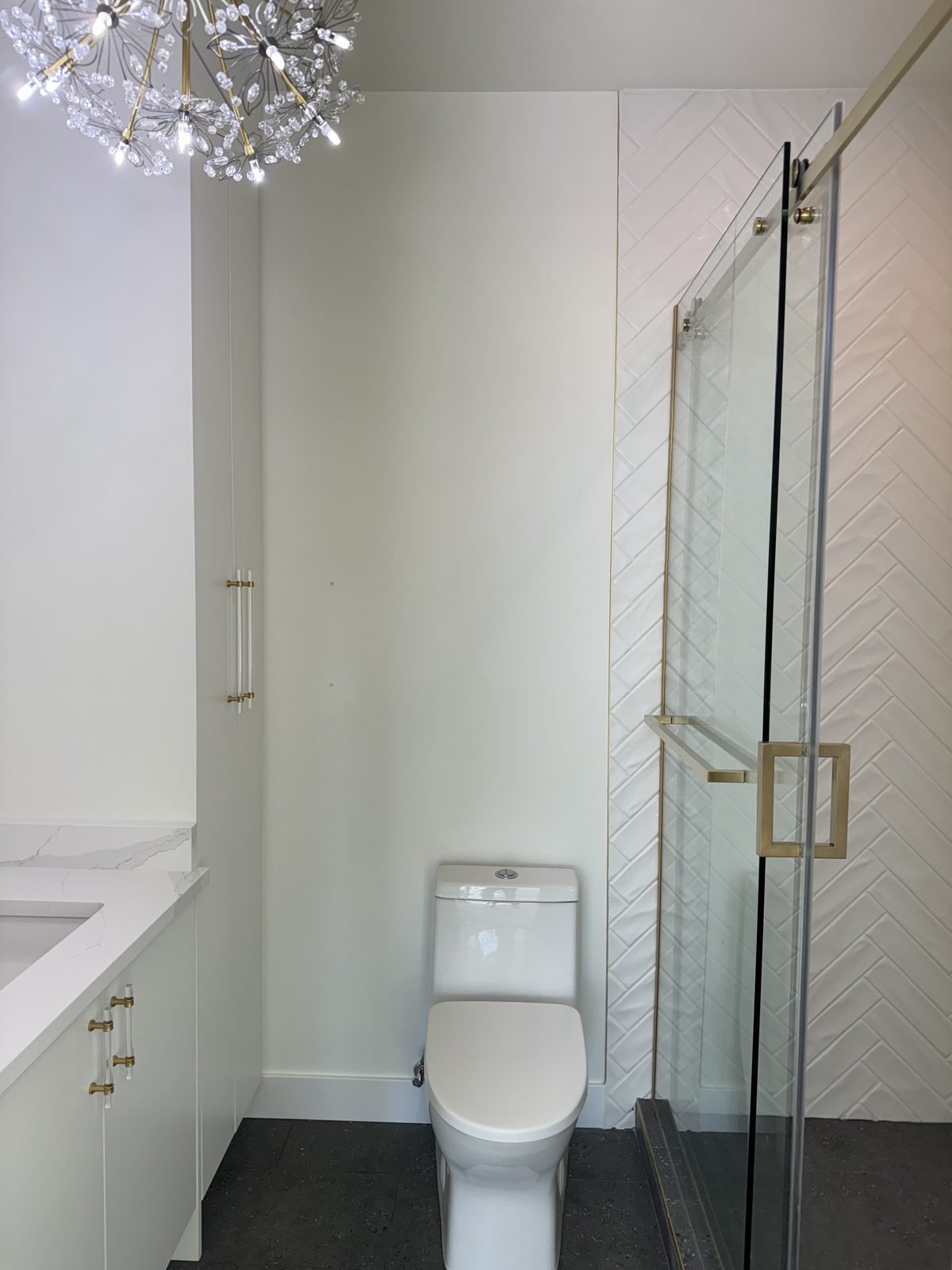 West End condo ensuite with a walk-in shower, white herringbone tile, brushed gold fixtures and a chandelier