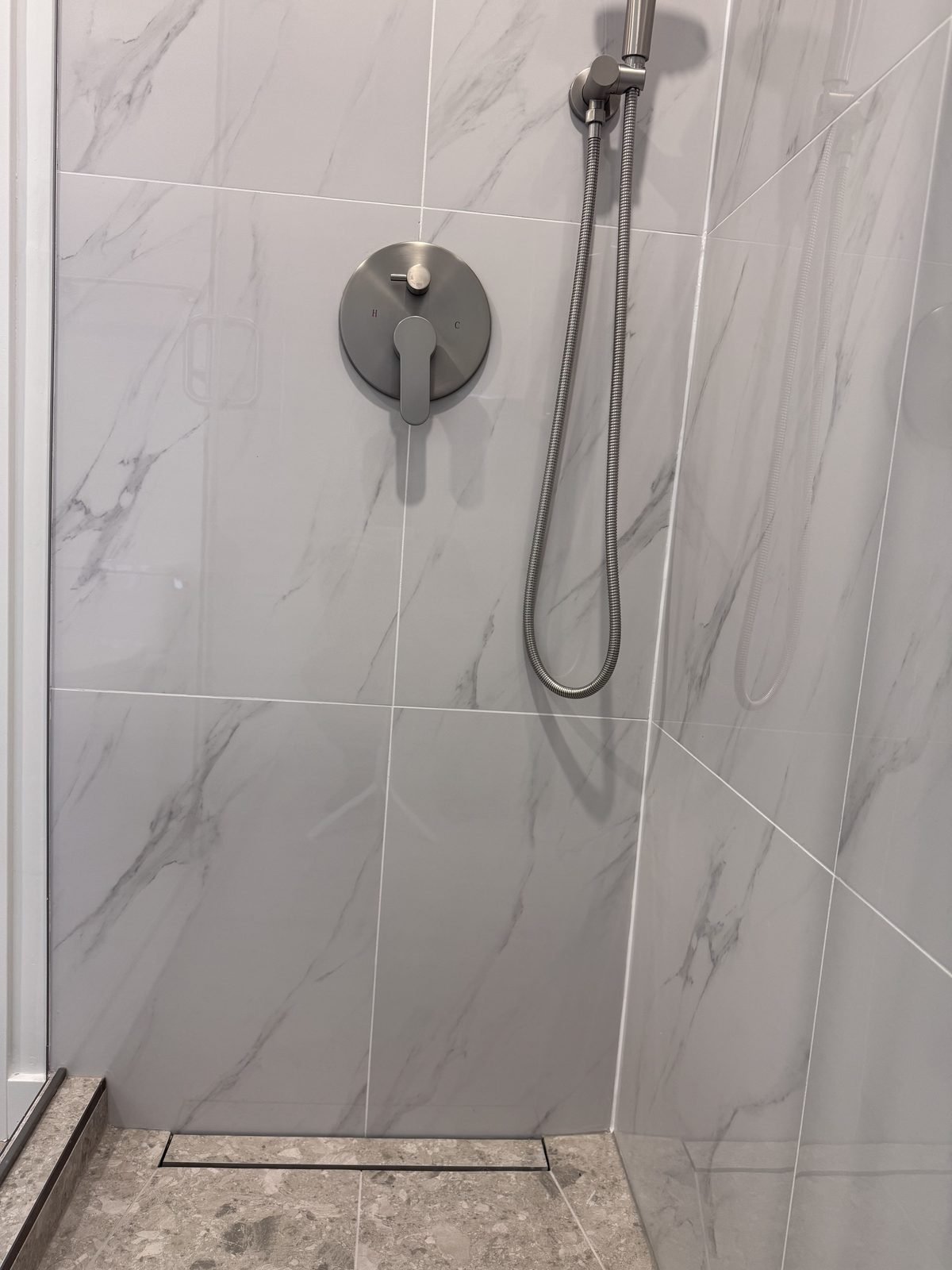 After: walk-in shower with a linear drain, marble-look porcelain walls and terrazzo-look floor tile in a West End condo ensuite