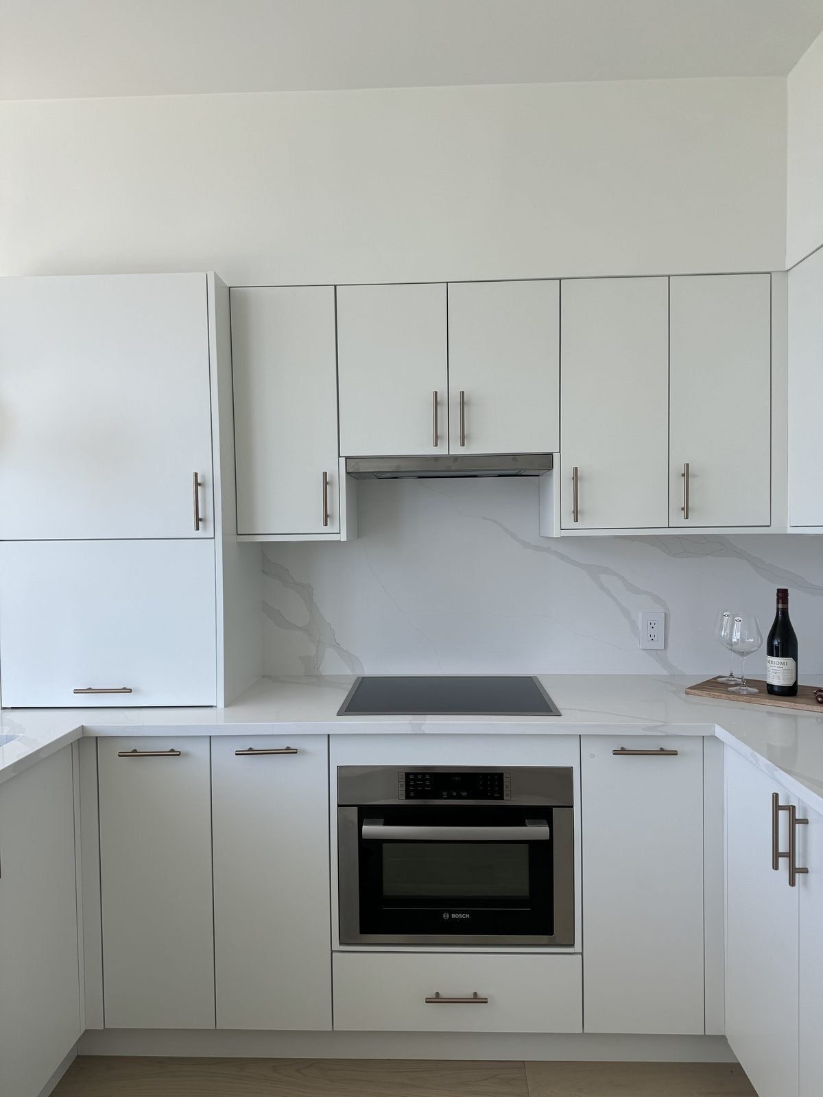 Bosch wall oven and cooktop under white cabinets with a full-height quartz backsplash in a West End condo kitchen