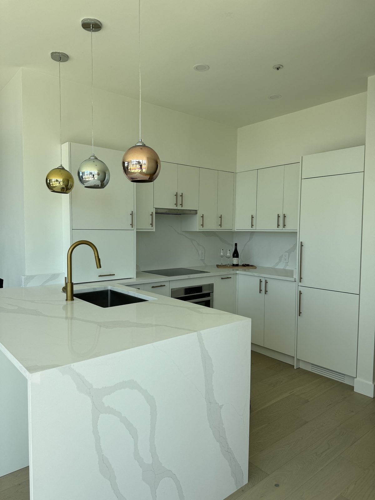 Quartz waterfall island with an undermount sink and gold, silver and copper glass pendants in a West End, Vancouver condo kitchen