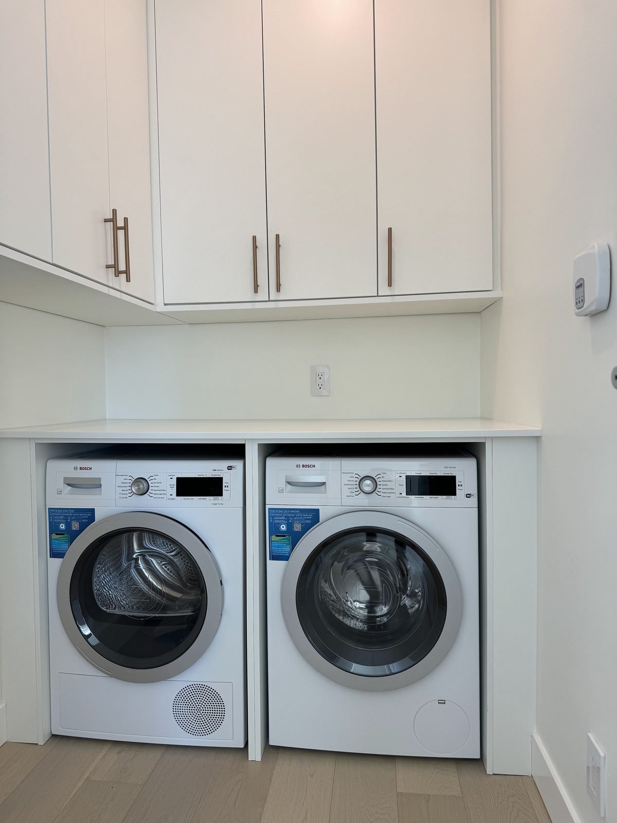 After: expanded laundry room with a side-by-side Bosch washer and dryer, counter and white upper cabinets in a West End condo