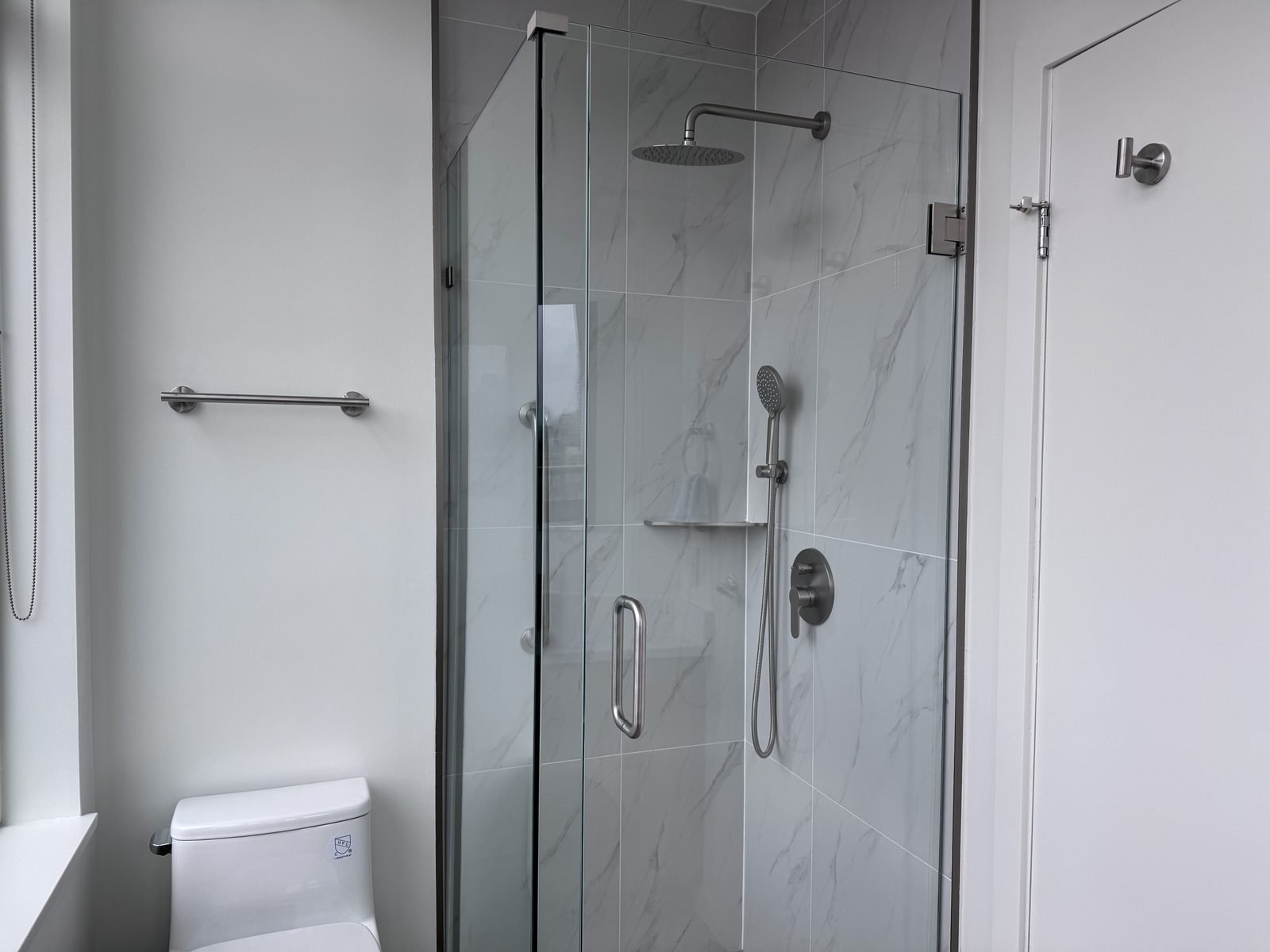 Main bathroom walk-in shower with a frameless glass door, rain head and marble-look tile in a West End condo