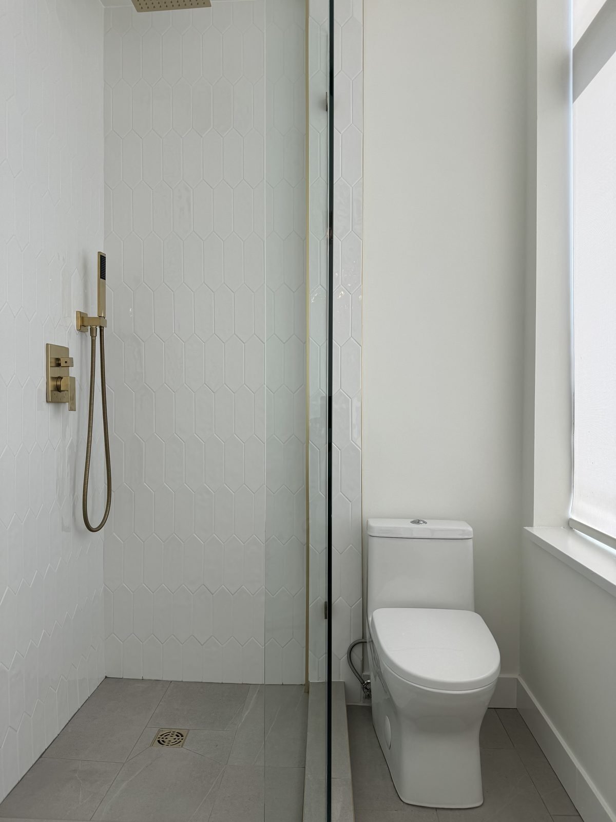 Main bathroom with a walk-in shower, white tile and a one-piece toilet beside the window in a West End condo