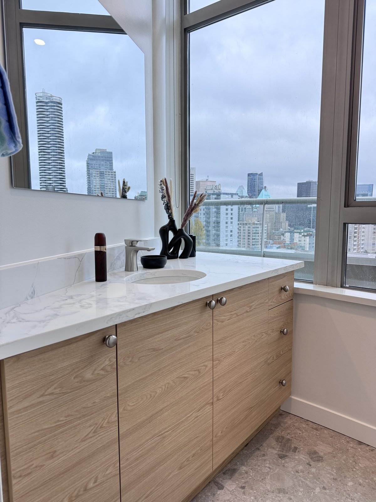 Main bathroom wood-grain vanity with a quartz top beside a window with city views in a West End, Vancouver condo