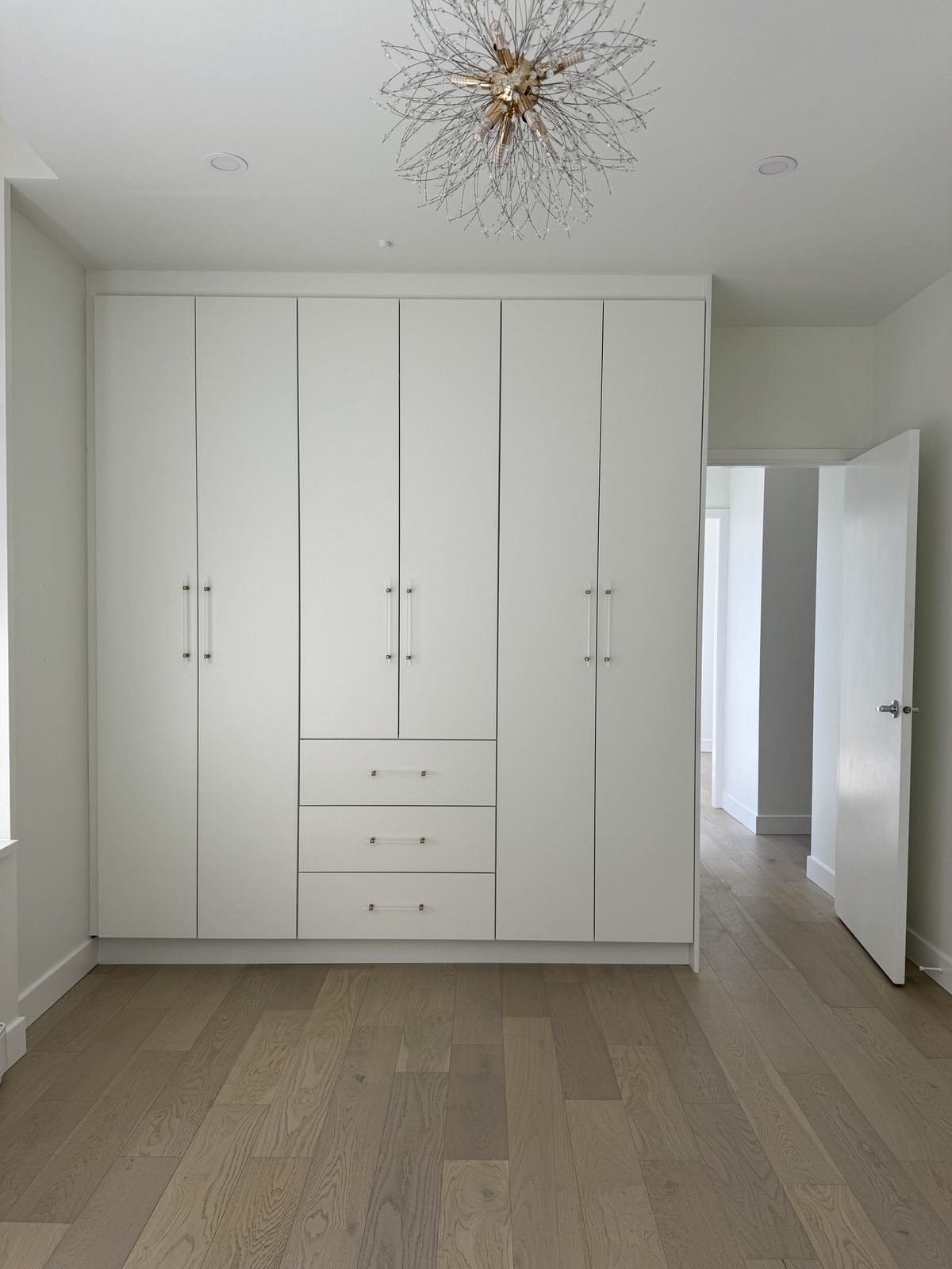 Primary bedroom with a custom white built-in wardrobe, drawers and a chandelier in a West End condo